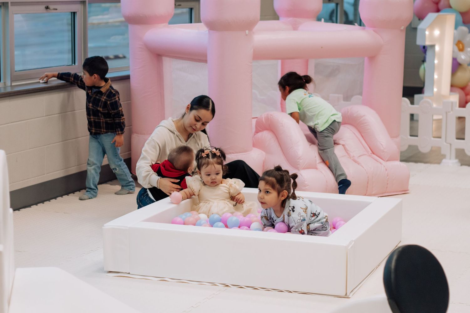 Children playing in a pink ball pit with bounce castle at birthday party celebration.