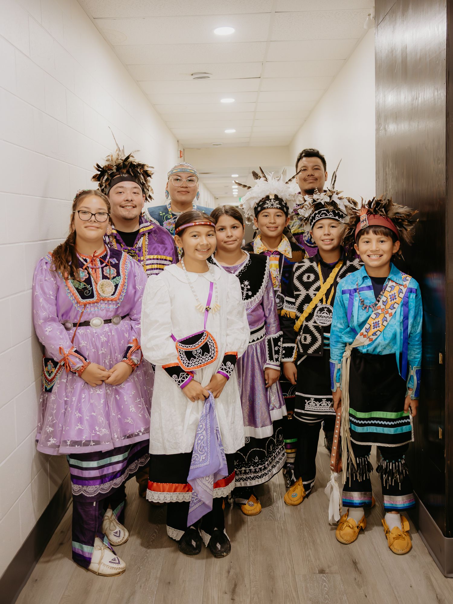 A group wearing traditional regalia and cultural dress poses together in a hallway.
