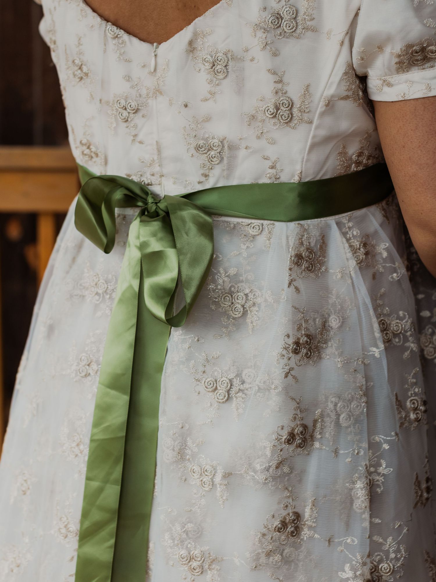 Close-up of a white floral embroidered wedding dress with a sage green satin ribbon bow at the waist.