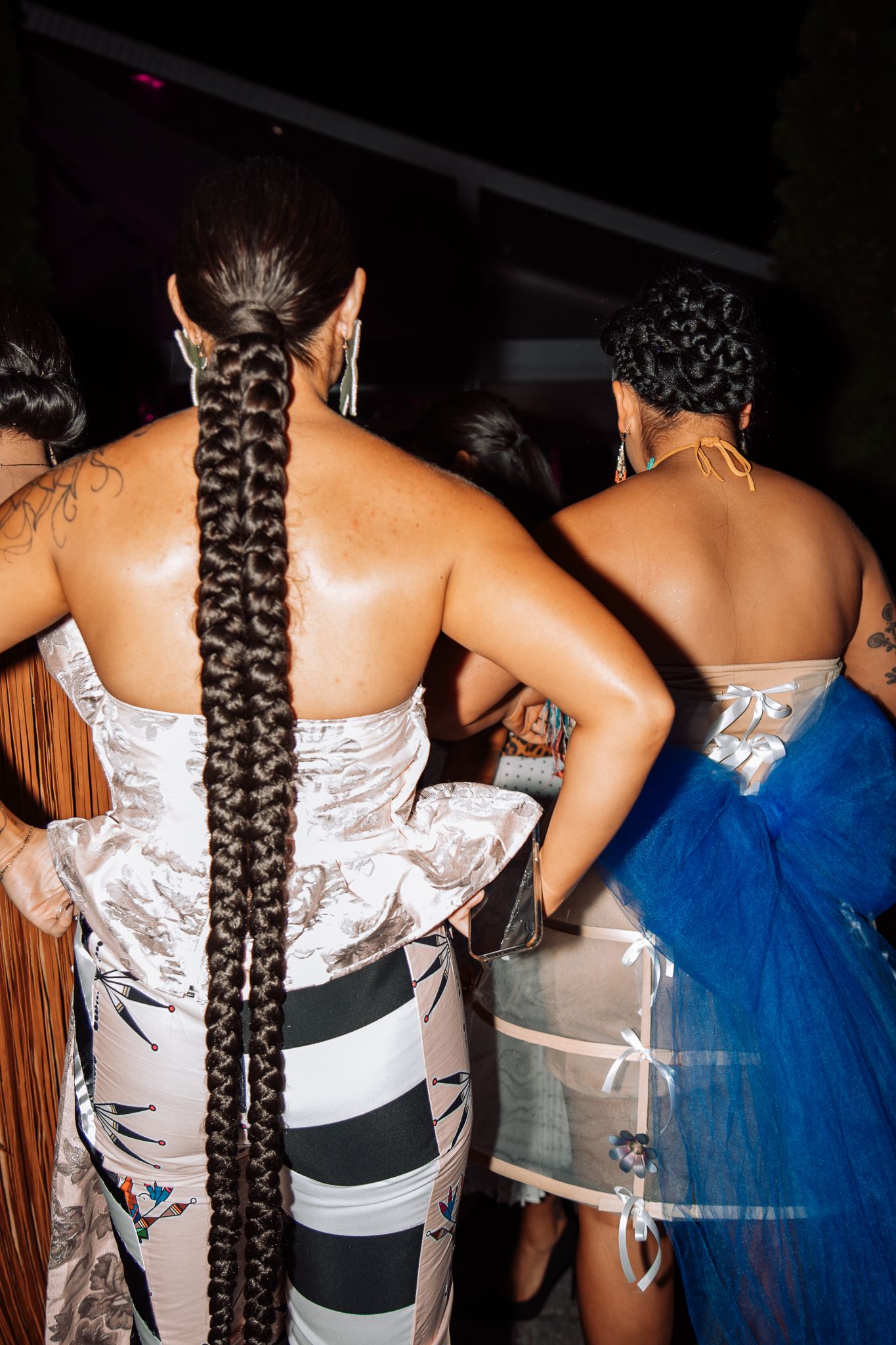Close-up view of intricate braided hairstyles and dress details on fashion models from behind.