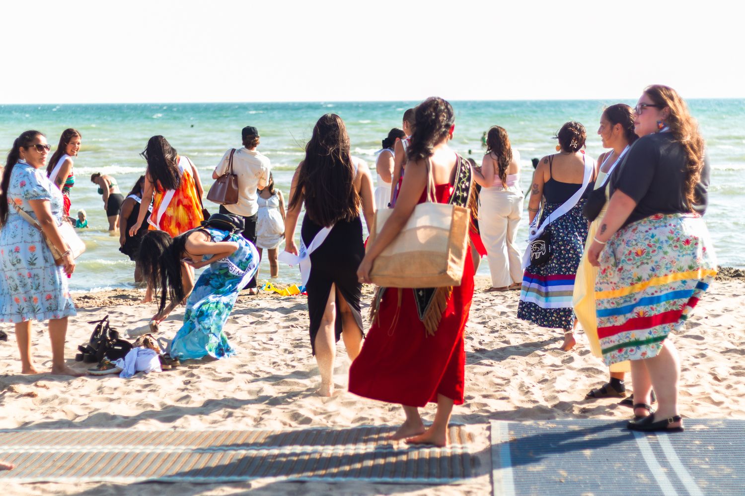 A group of people in colorful dresses gather on a sunny beach for a celebration.