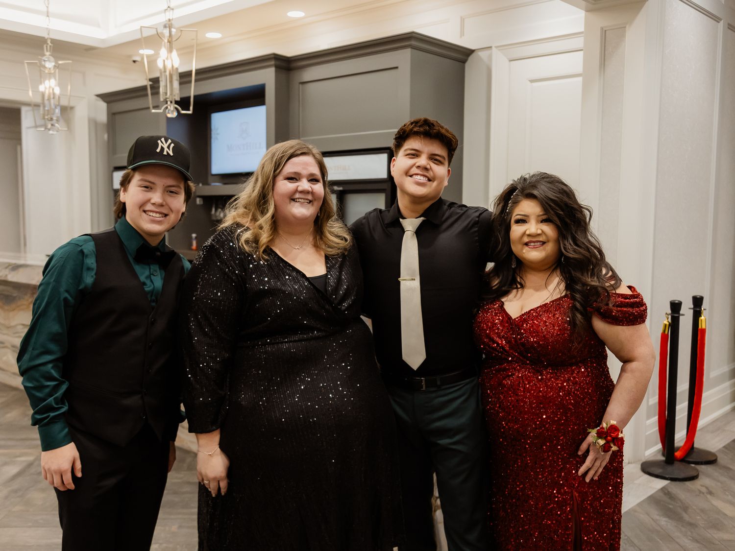 Four people dressed in formal attire pose together at an elegant holiday party.