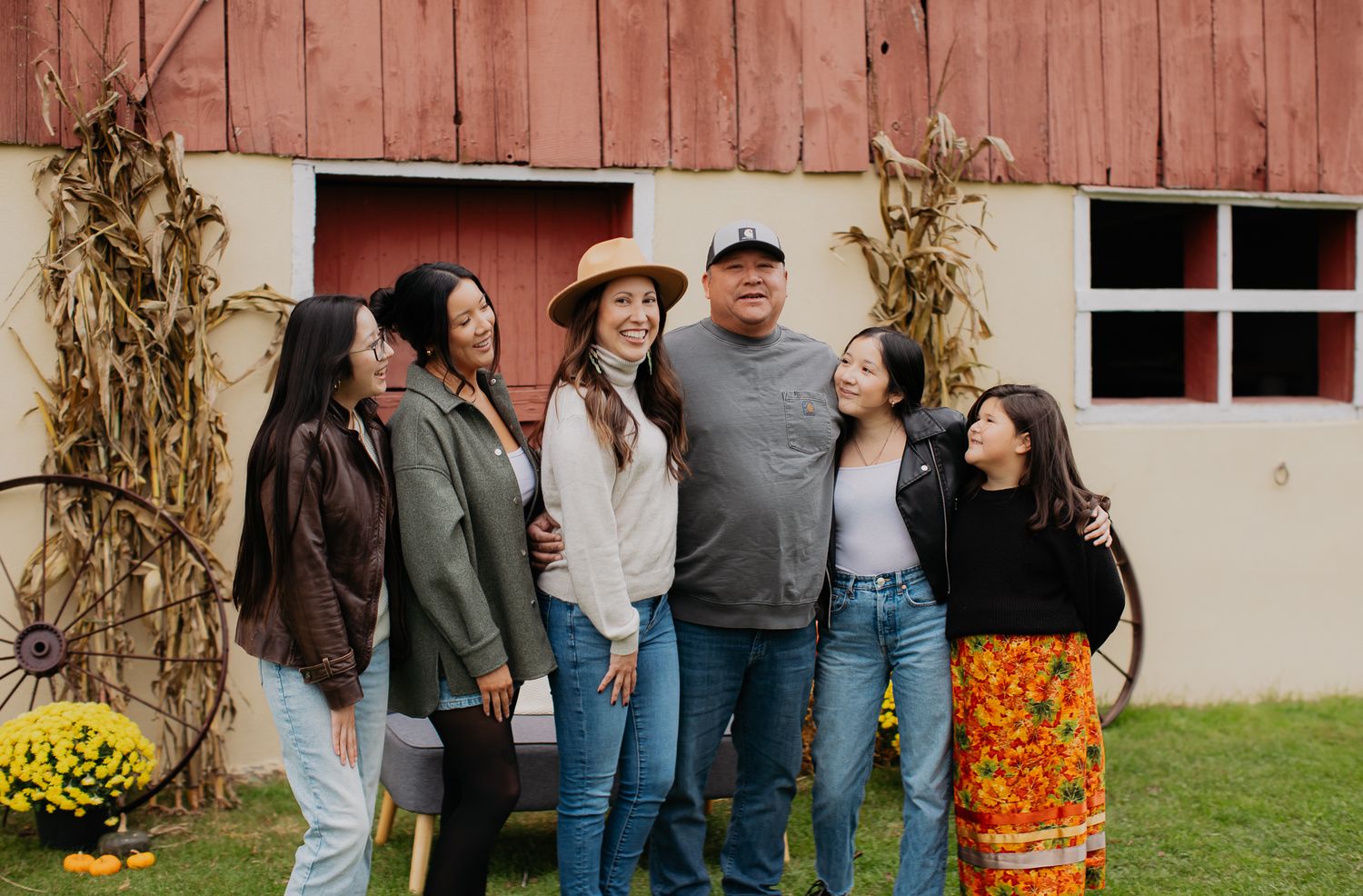 Group gathering outside a rustic red barn decorated with dried cornstalks.
