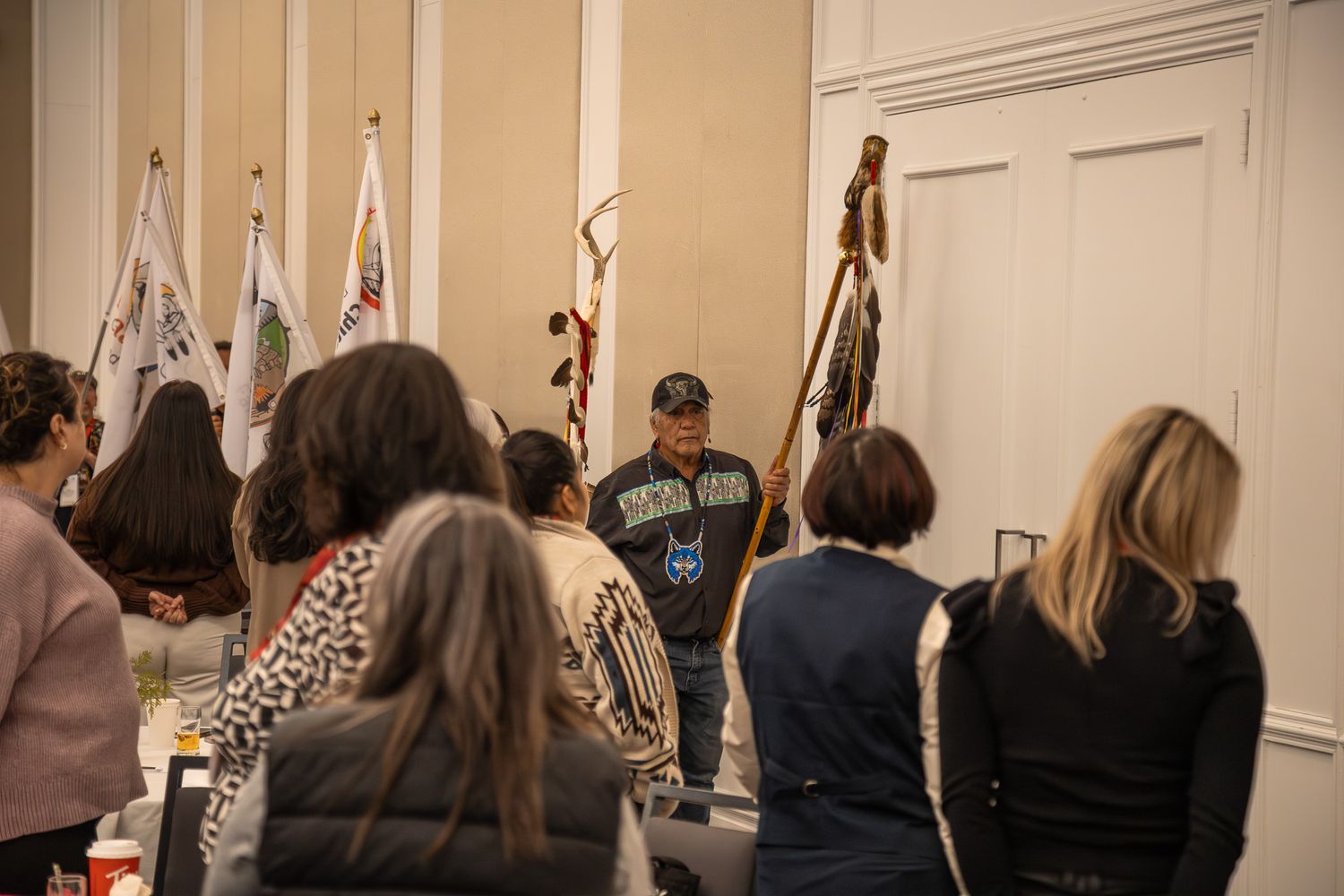 Row of attendees standing against a beige wall at an indoor event.