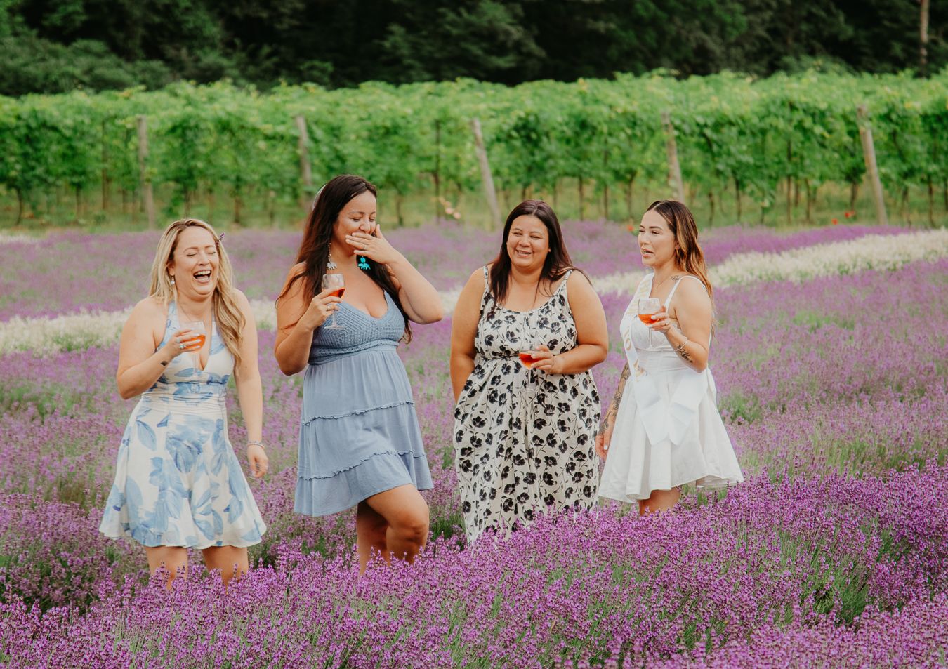 Friends laughing together in flowing dresses amid purple lavender field.