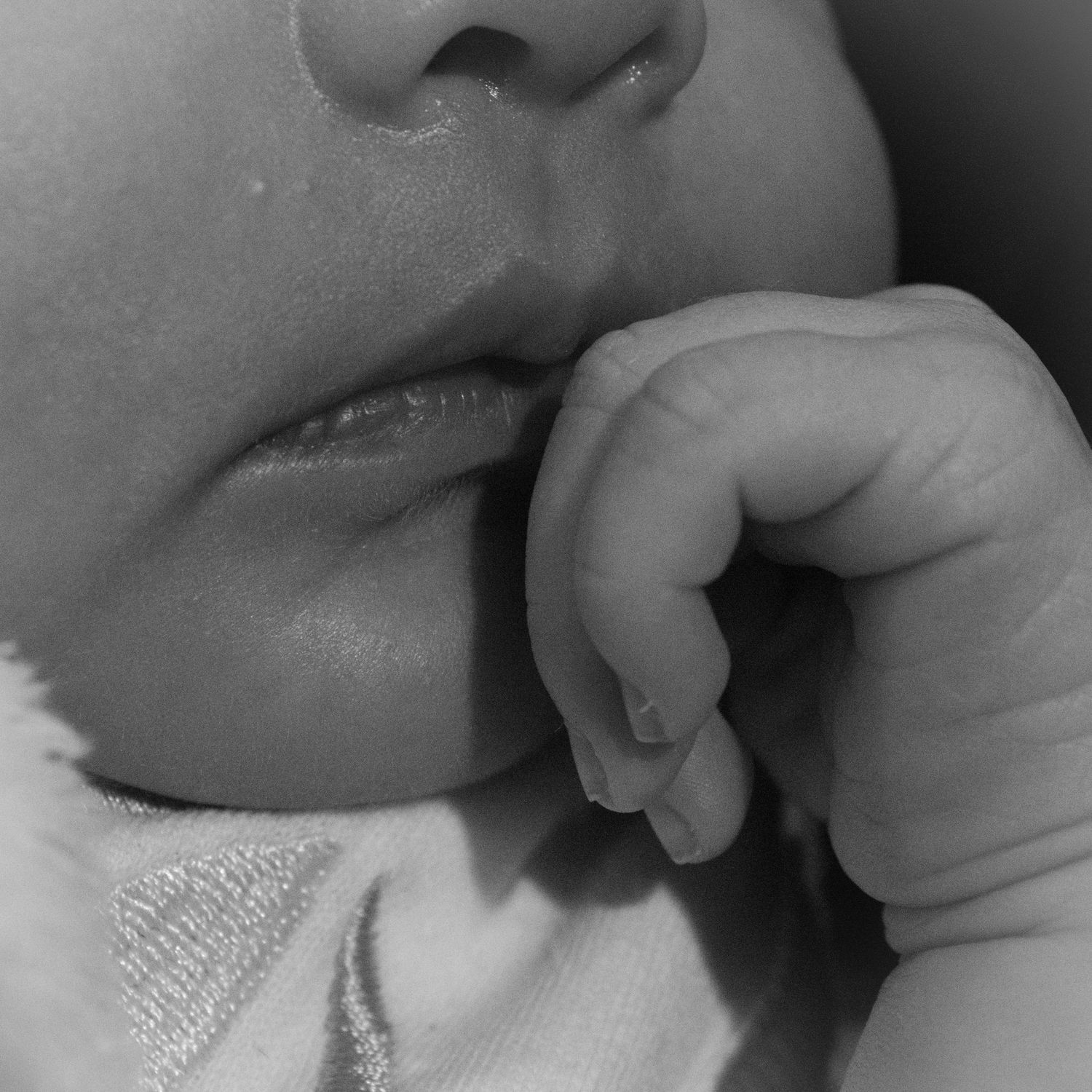Macro shot of baby's mouth and tiny hand in black and white.