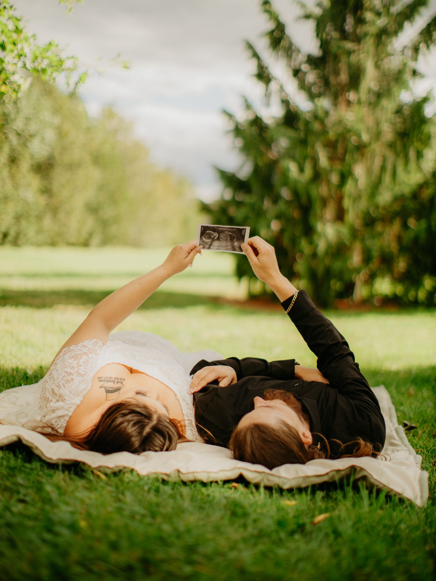 Two people lying on a blanket outdoors holding up a photo while enjoying a sunny day.