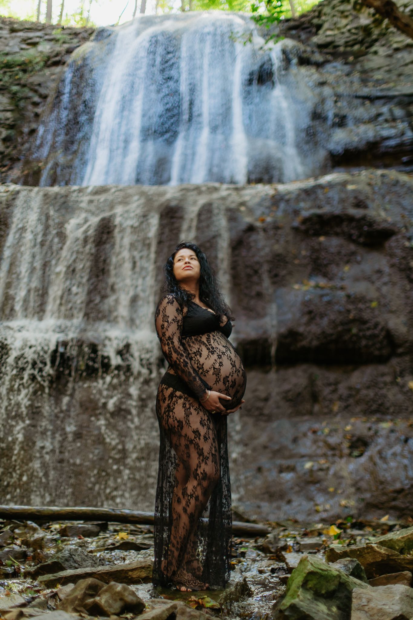 Maternity photos captured against a stunning waterfall backdrop in natural lighting.