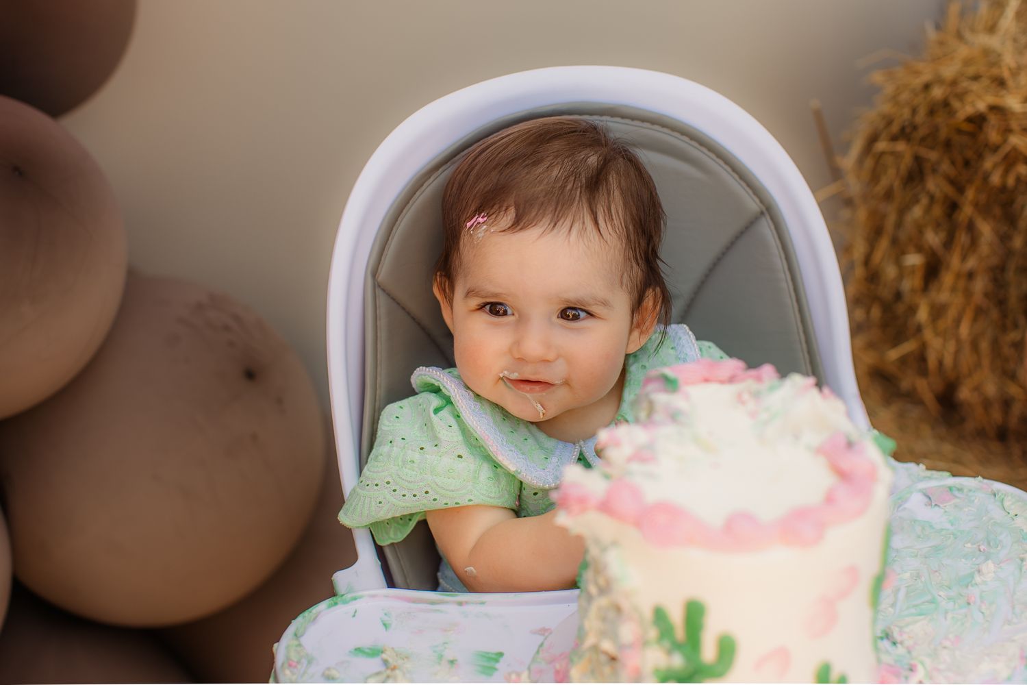 Baby girl in high chair with pink and white first birthday smash cake at rodeo themed party.
