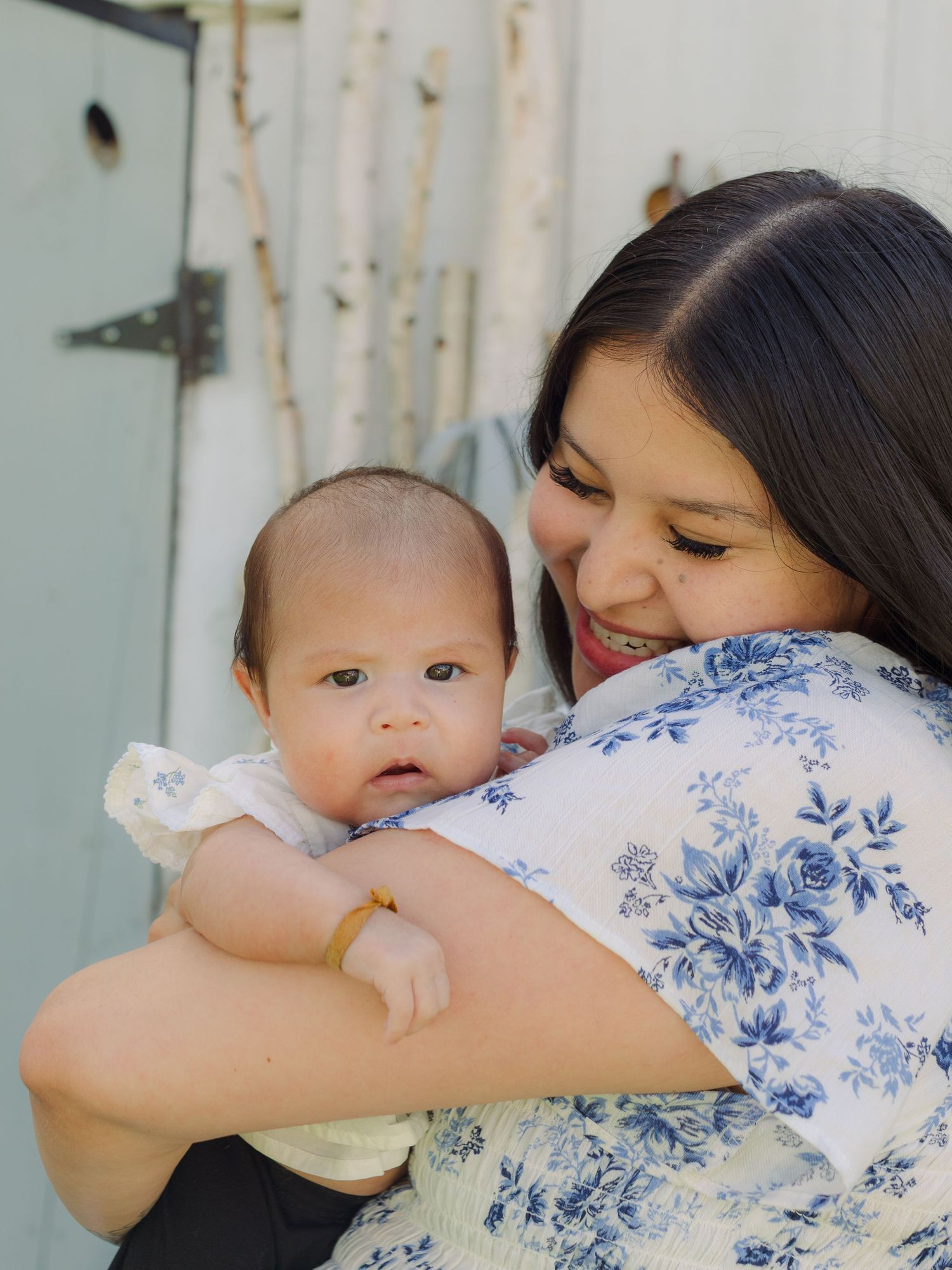Smiling woman in floral blouse tenderly holds newborn baby close outdoors.