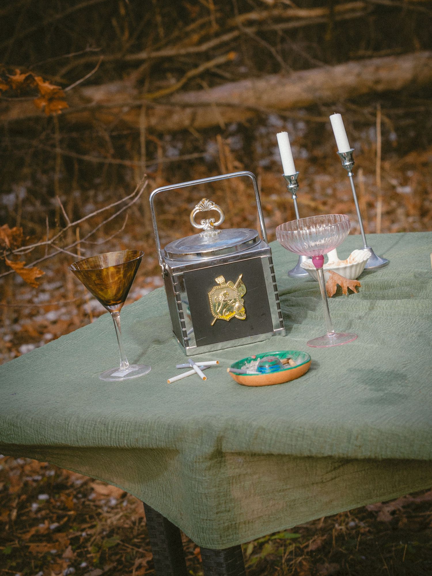 Vintage table setting with candles, wine glasses, and decorative box in an autumn forest.
