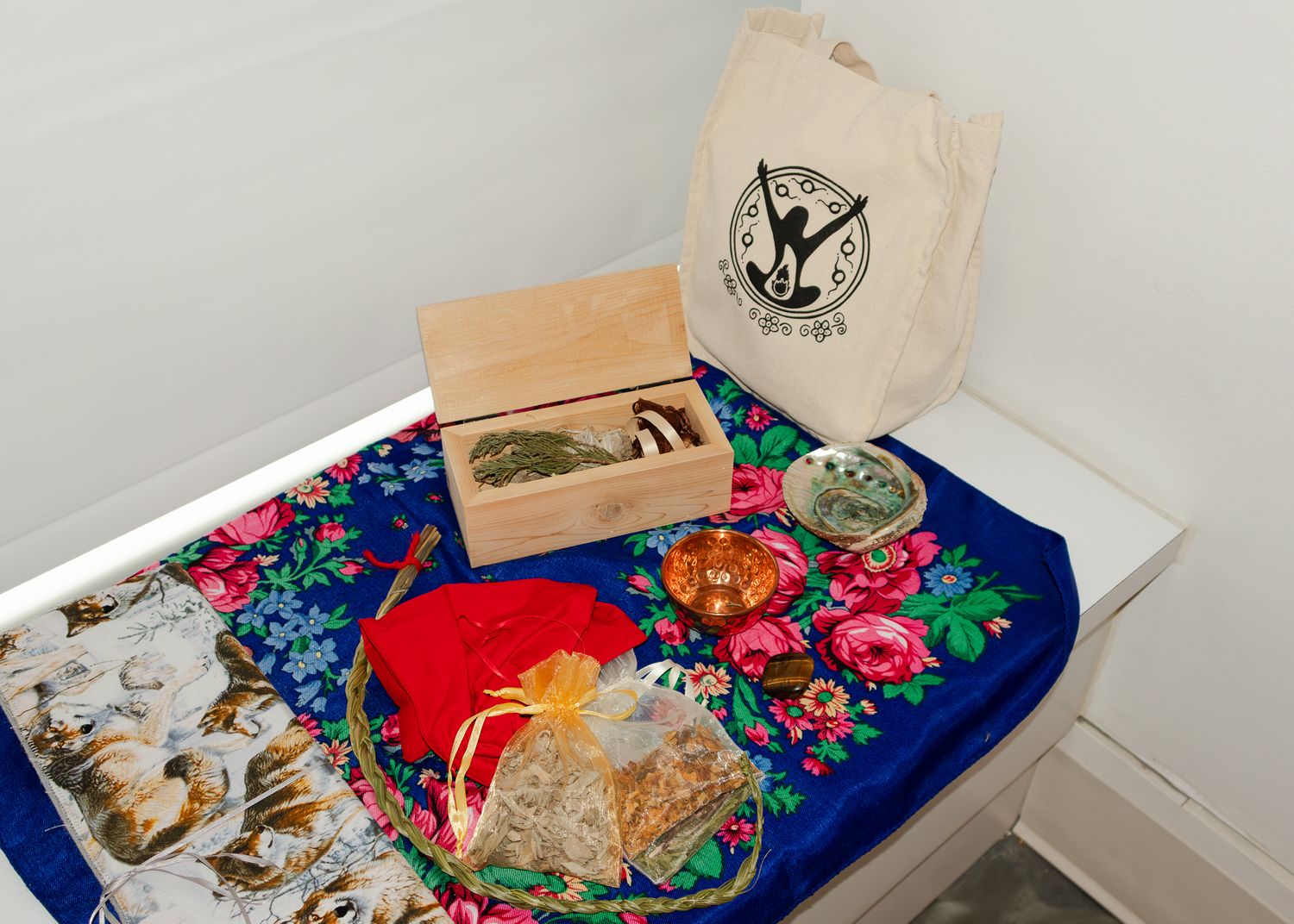 A wooden box, tote bag, and colorful wrapped gifts arranged on a floral cloth on a white surface.