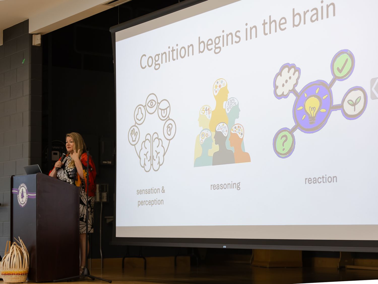 Female speaker presents cognition brain research slide at academic conference podium with illustrated projection screen.
