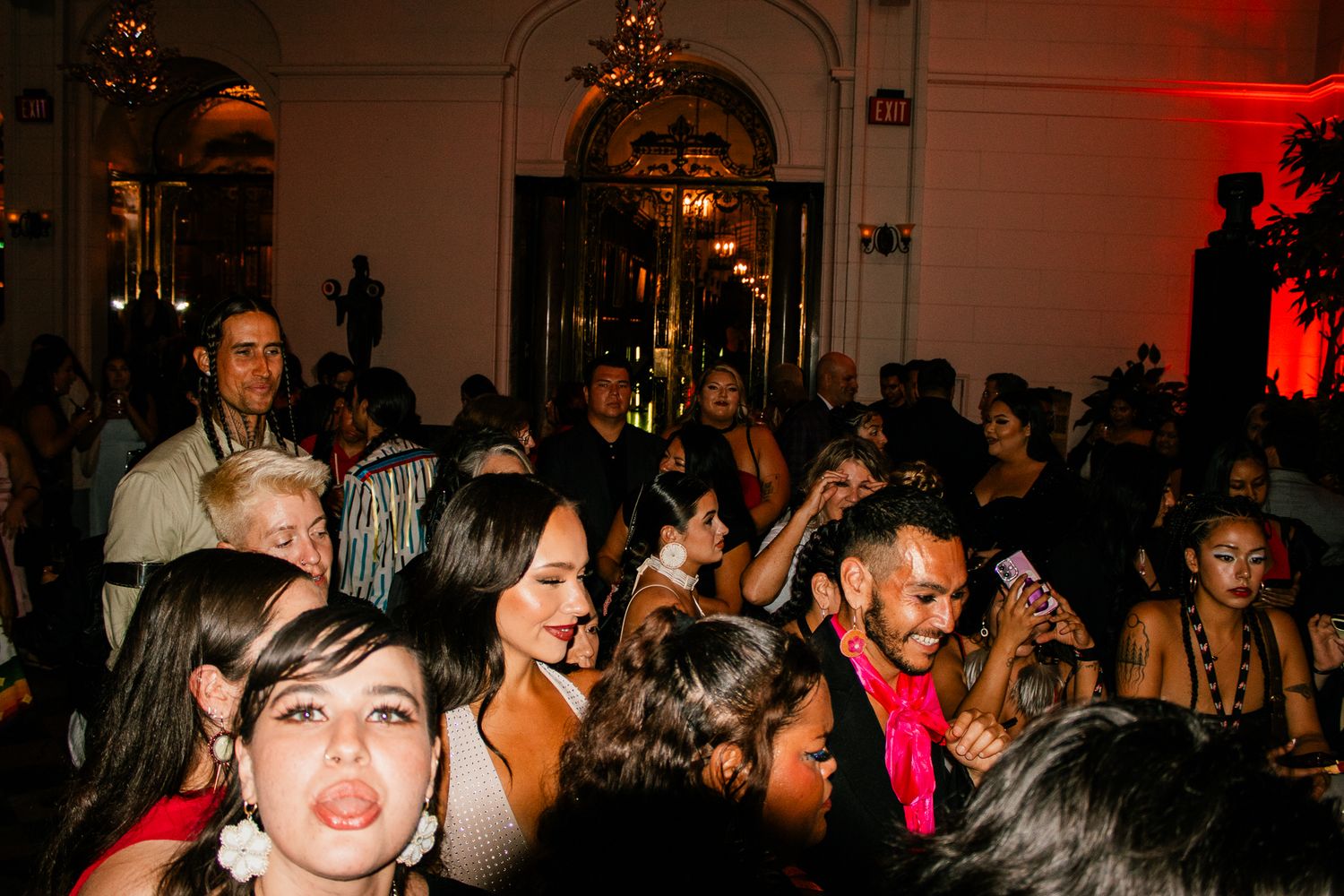 Crowded indoor party scene with guests dancing and socializing under dramatic red lighting.