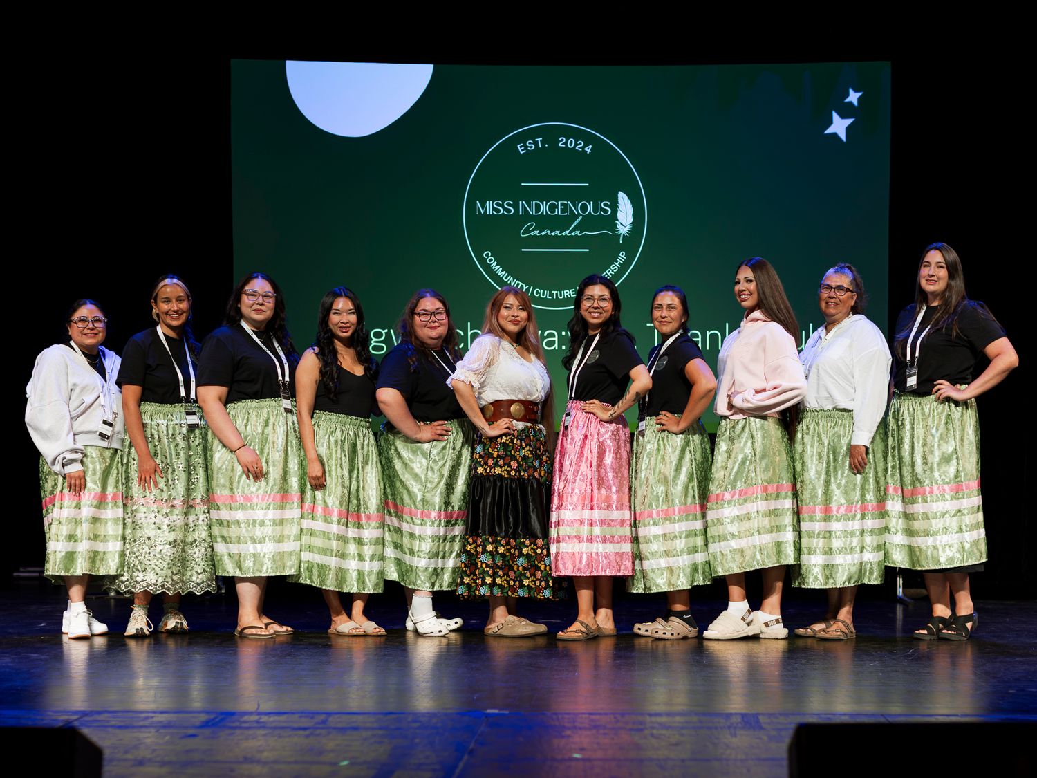 Group of Indigenous women in traditional green skirts on stage at Miss Indigenous Canada pageant.
