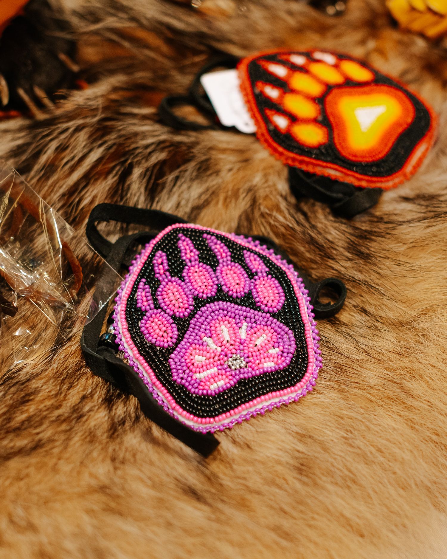 Handcrafted beaded hair clips featuring colorful bear paw designs in pink and orange on black, displayed on fur.