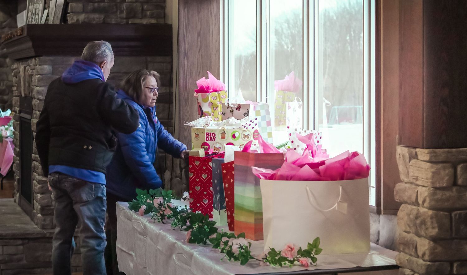 Guests browse pink birthday gifts and cake display at an indoor first birthday celebration.