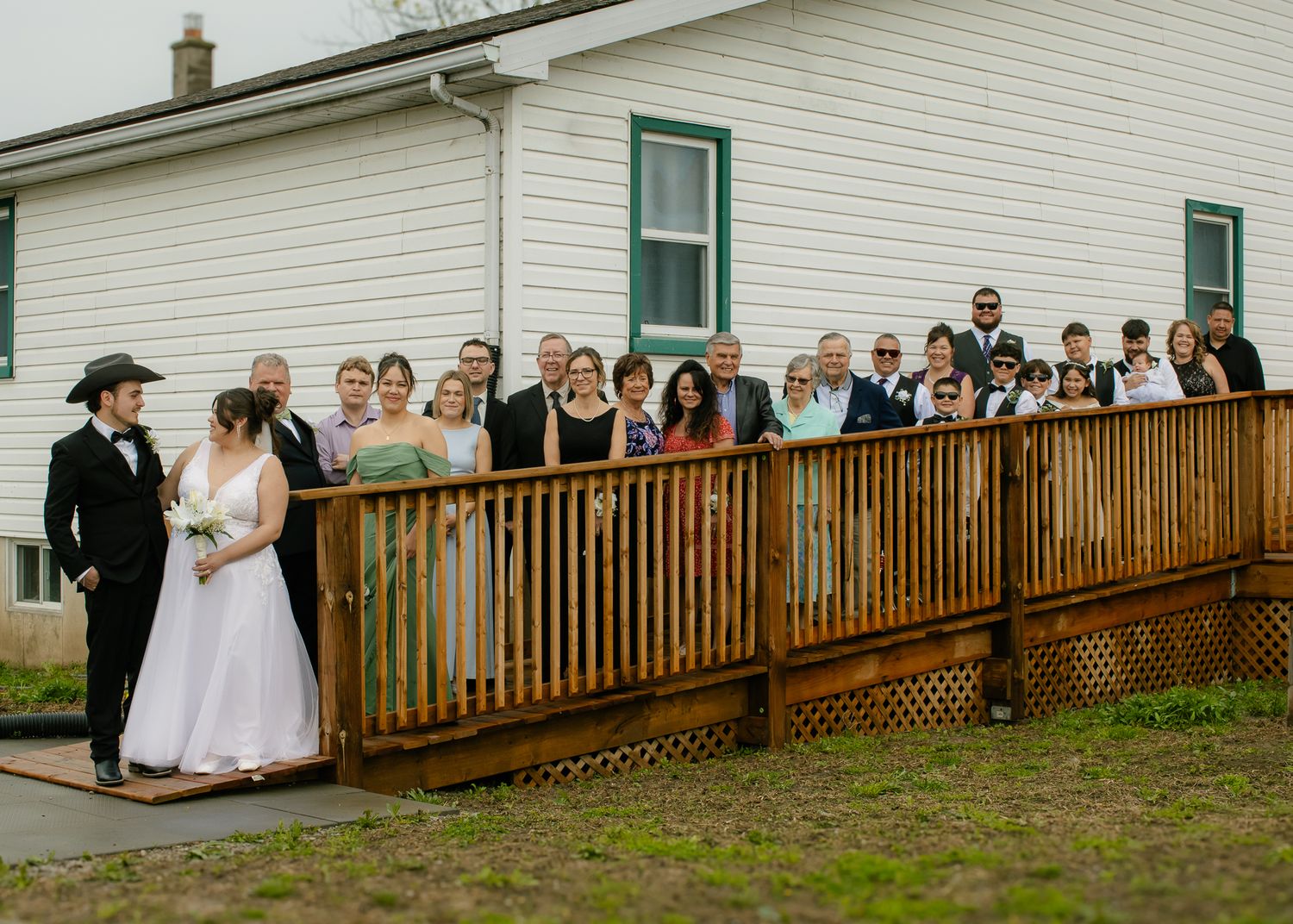 Wedding party posing on a wooden deck outside a white country church.