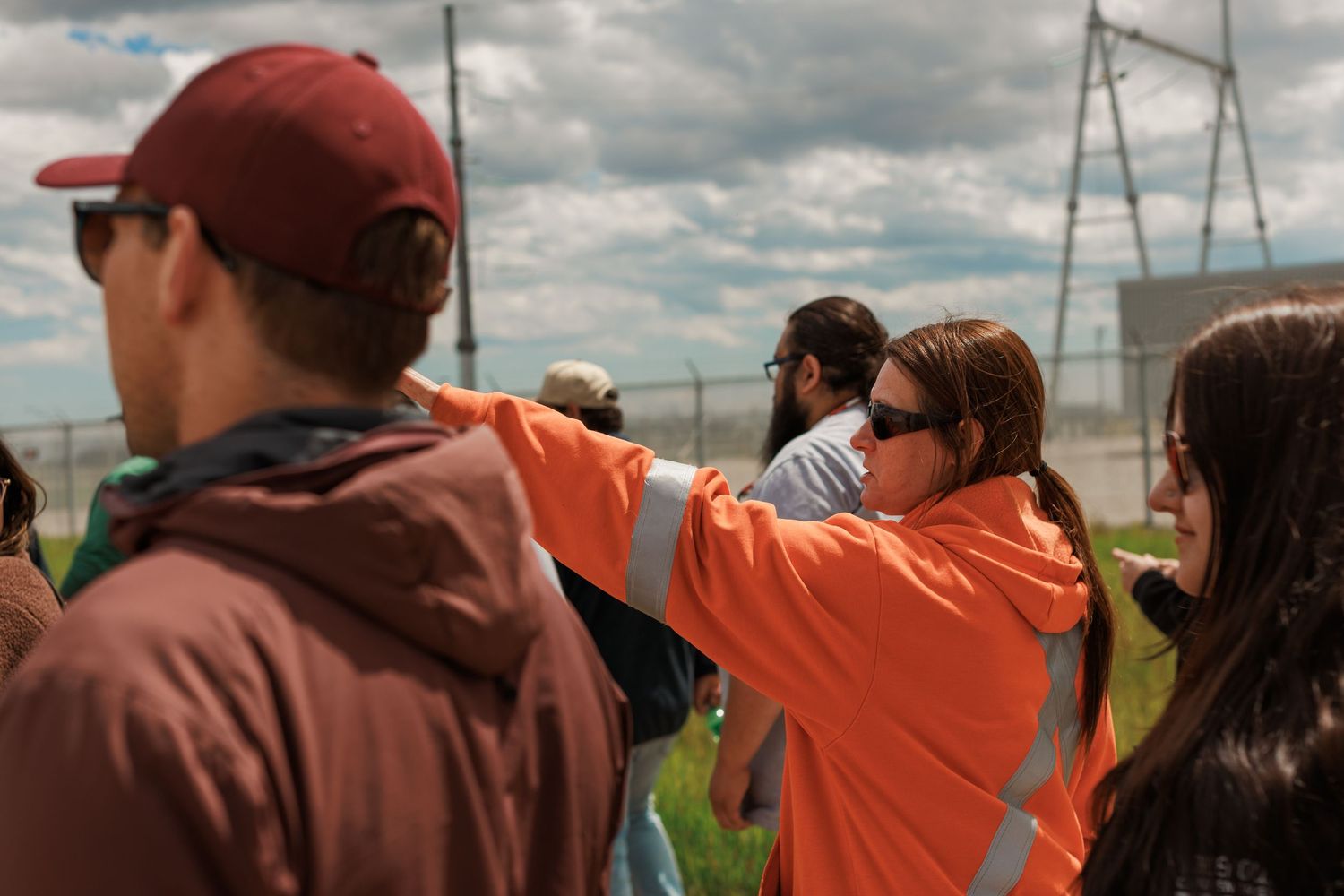 Person in orange high-visibility vest pointing during an outdoor Indigenous clean energy site tour.