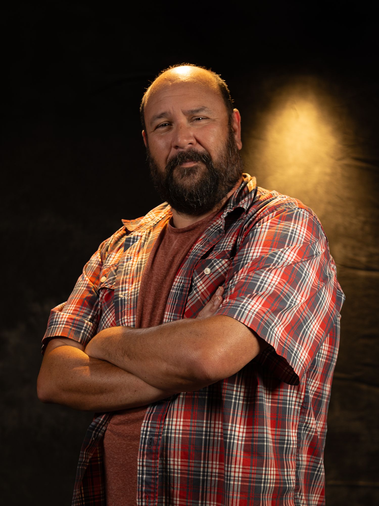 Casual portrait of person in plaid shirt and rust colored t-shirt against dark background.