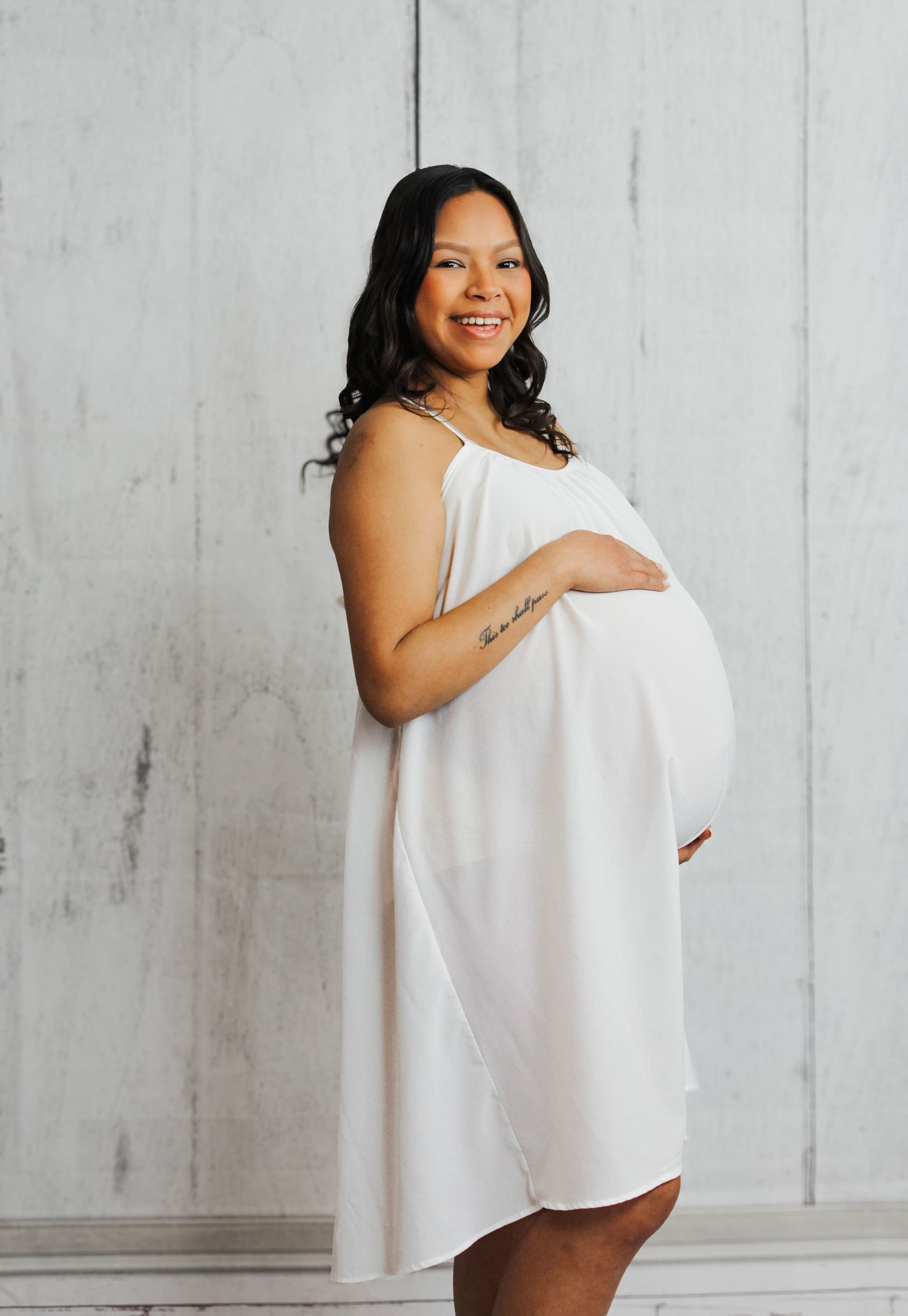 Joyful maternity session featuring white flowing dress against light background.