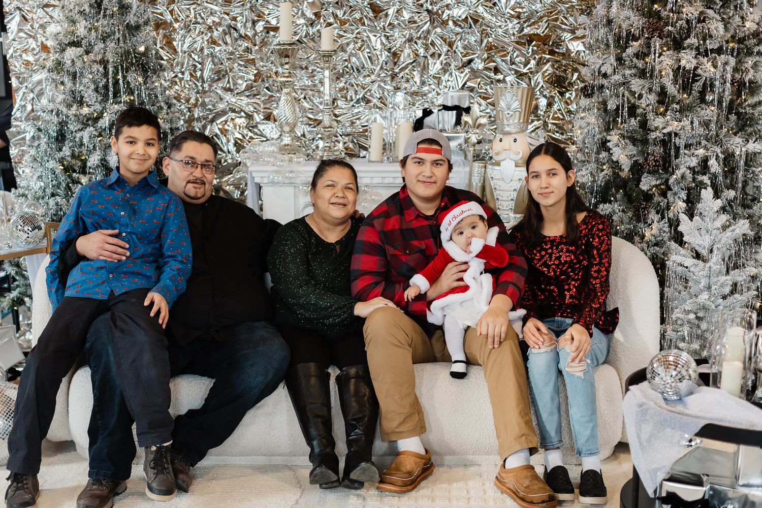 Family holiday portrait with winter backdrop showing multiple generations sitting together on a white couch.