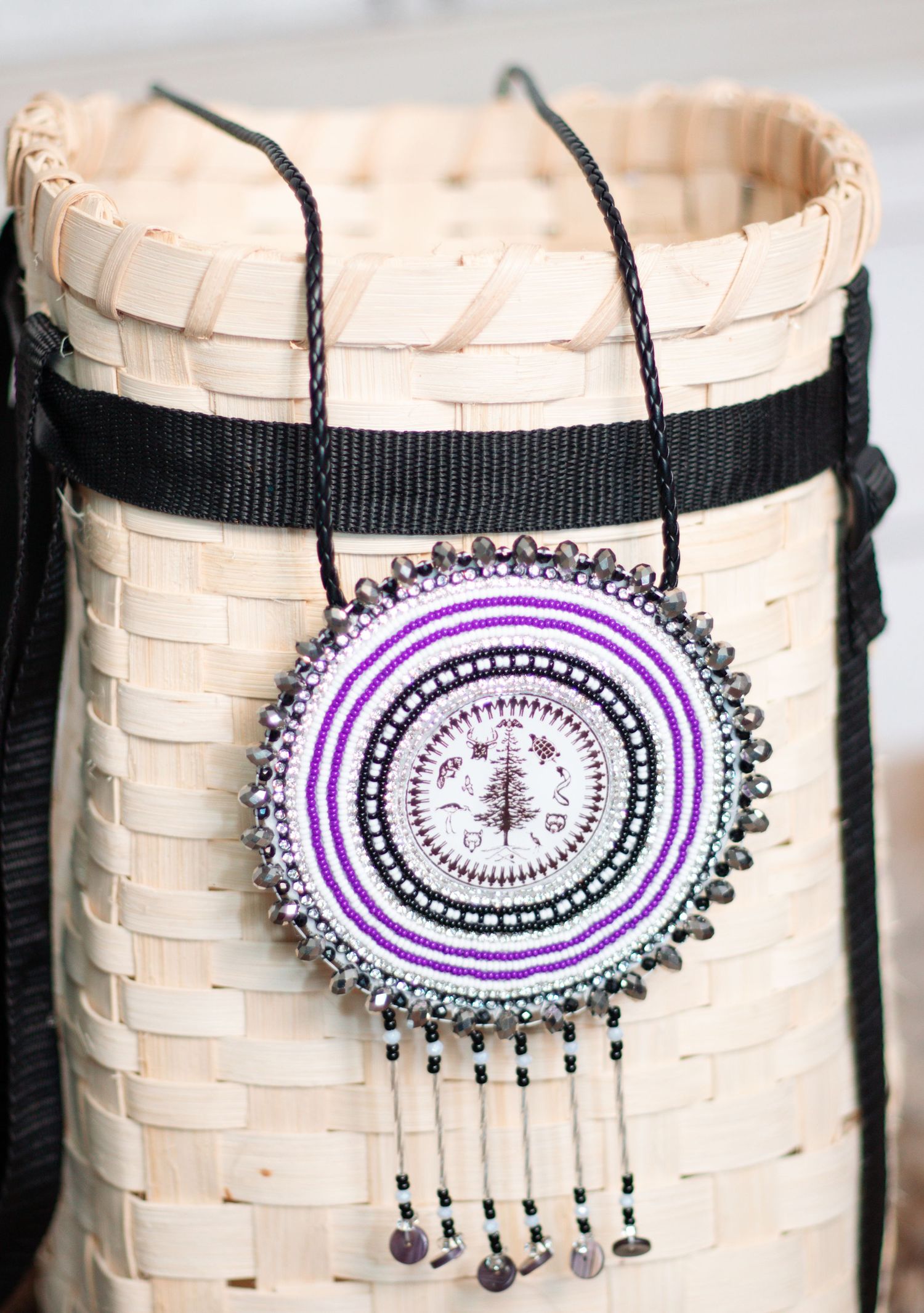 Beaded medallion necklace with purple and white circular pattern on birch bark basket.