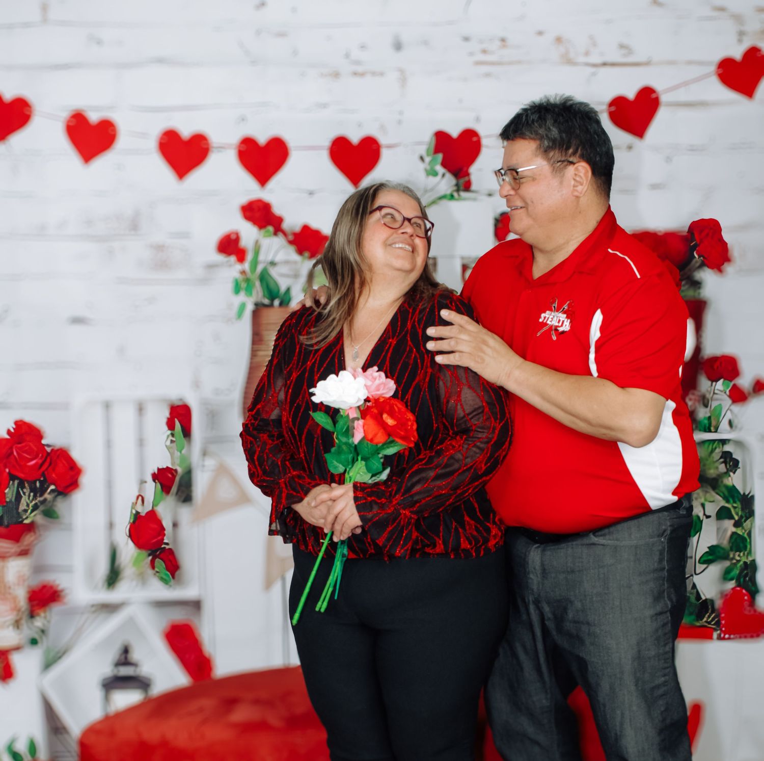 Romantic Valentine's photoshoot with red hearts, roses and white brick wall background.