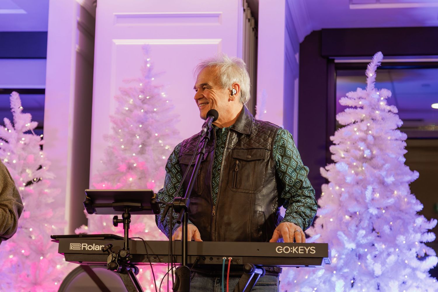 Band members playing instruments on stage with white Christmas trees and purple lighting.