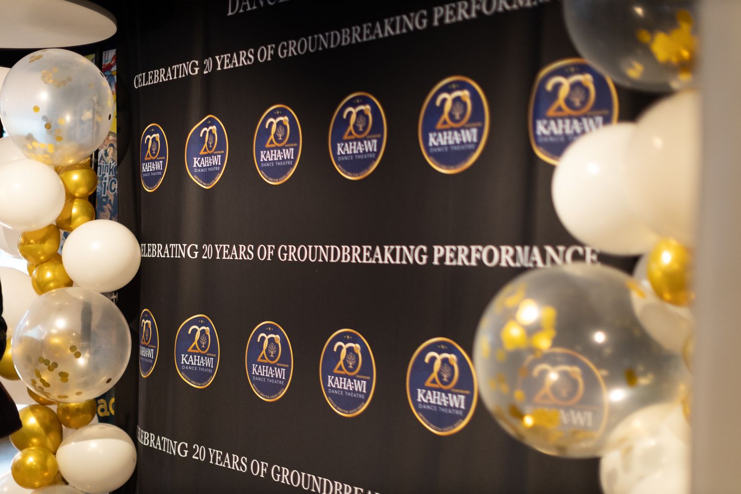 Event backdrop with repeating 20th anniversary logos and gold balloons for celebration.