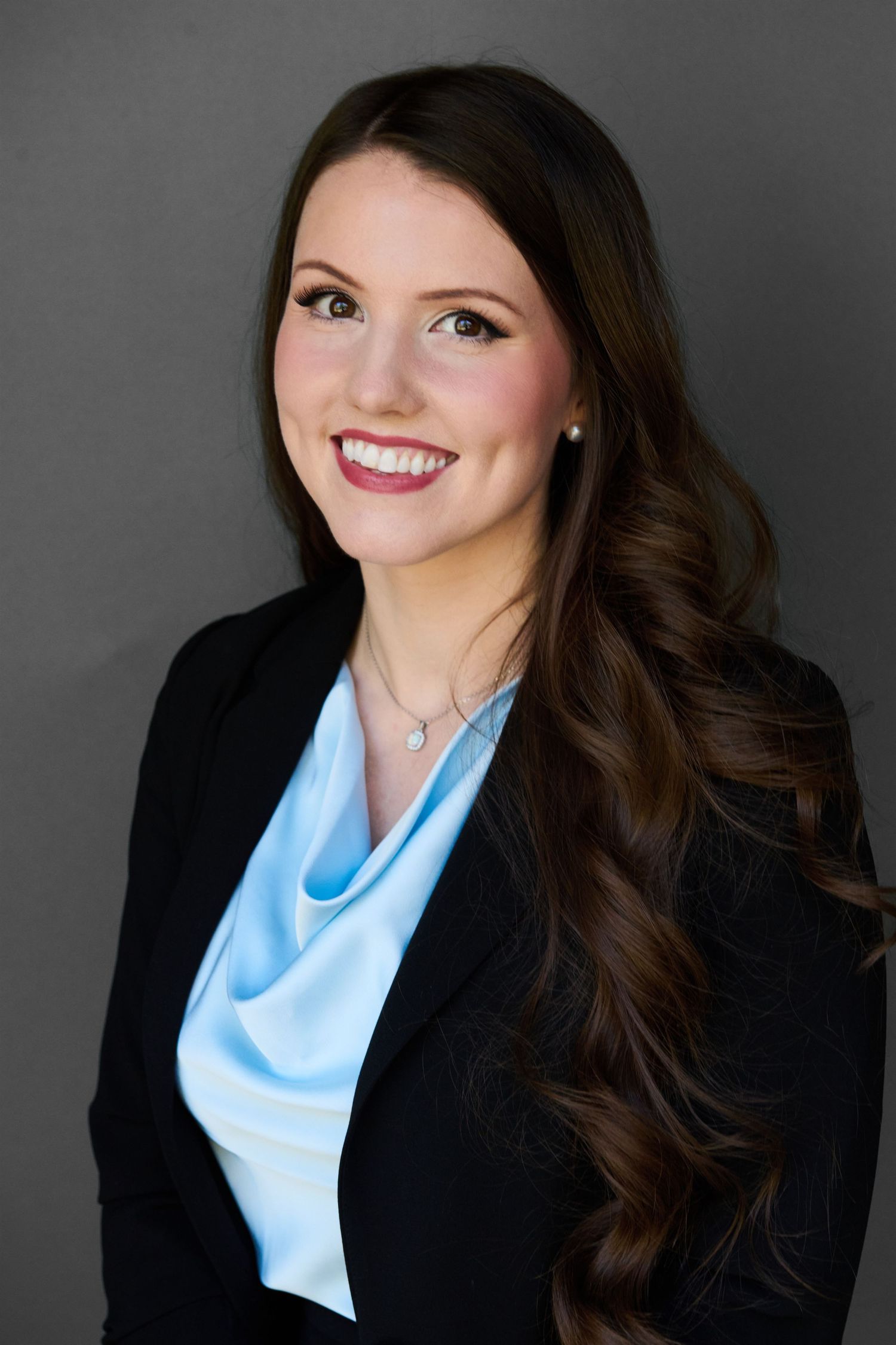 Professional woman in black blazer and blue top smiling for corporate headshot.