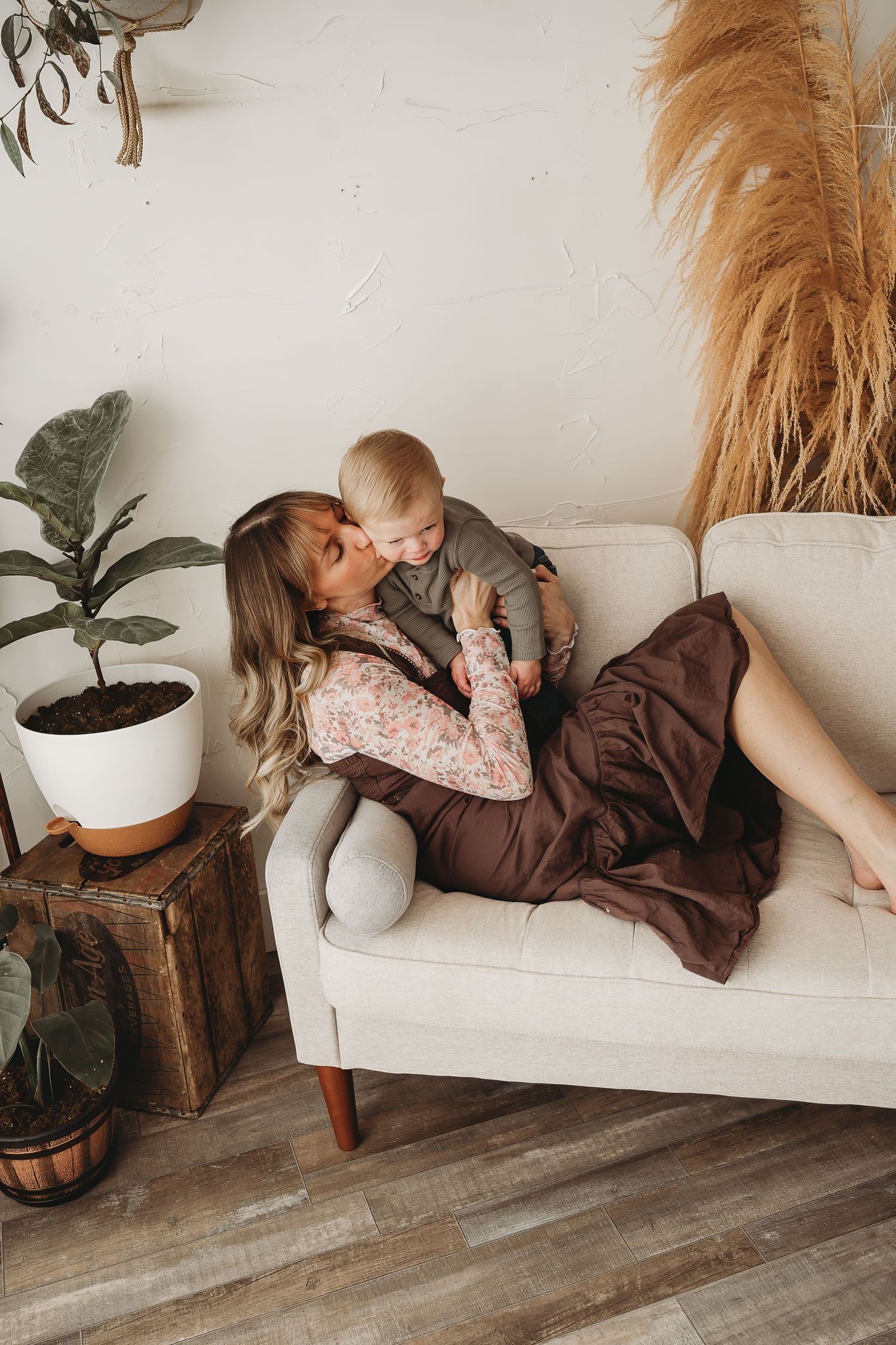 Blonde mother lying on a cream sofa kissing her baby in a boho-styled living room.