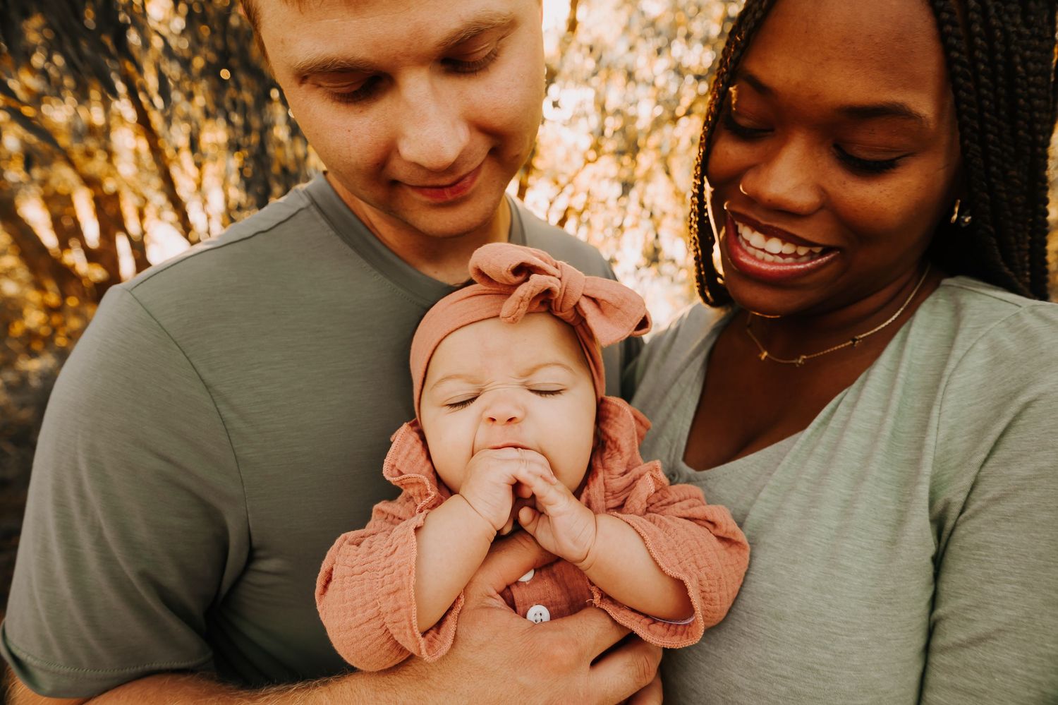 Smiling interracial couple lovingly holding their sleeping newborn baby girl outdoors.