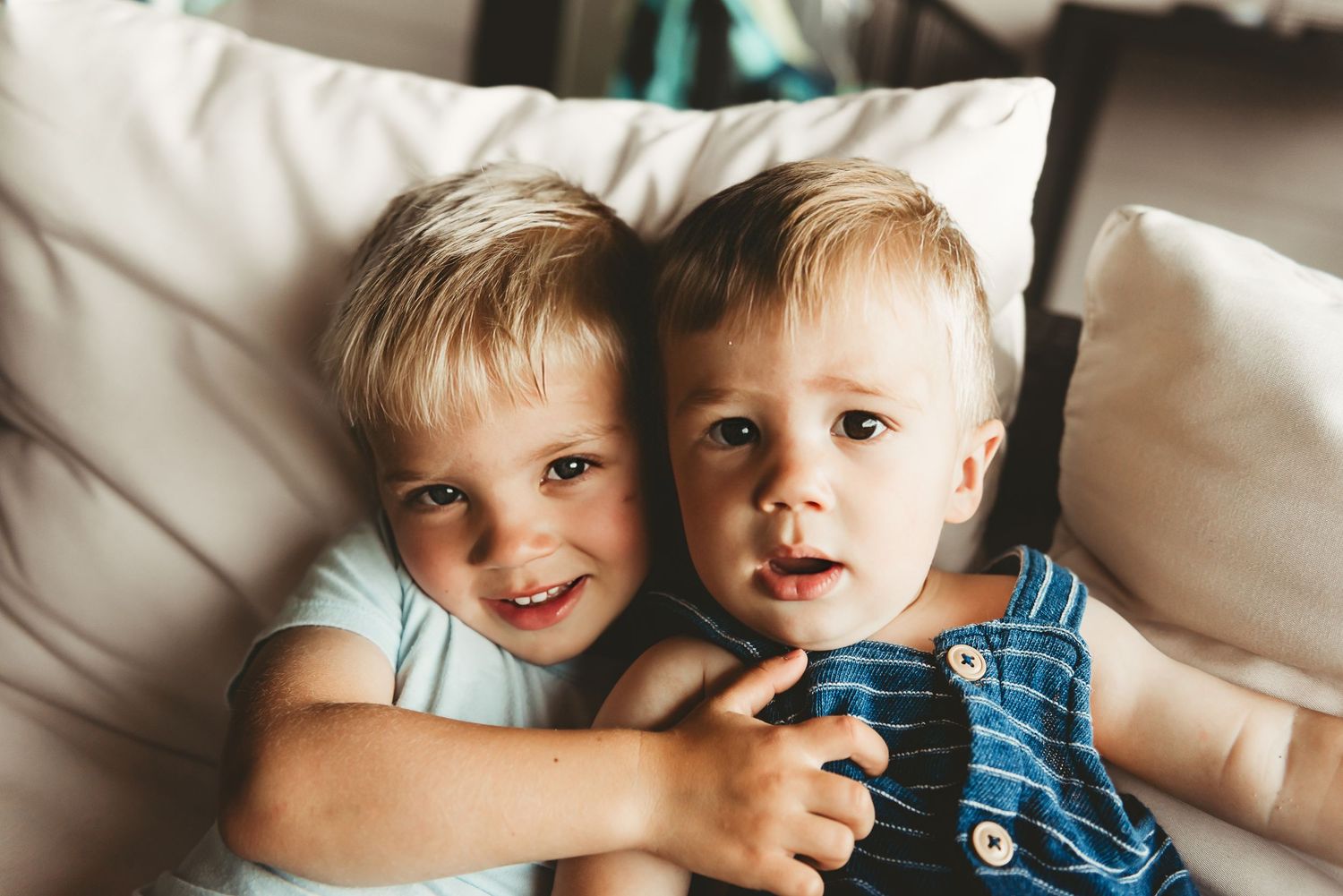 Two siblings sharing a sweet moment together on a white couch.