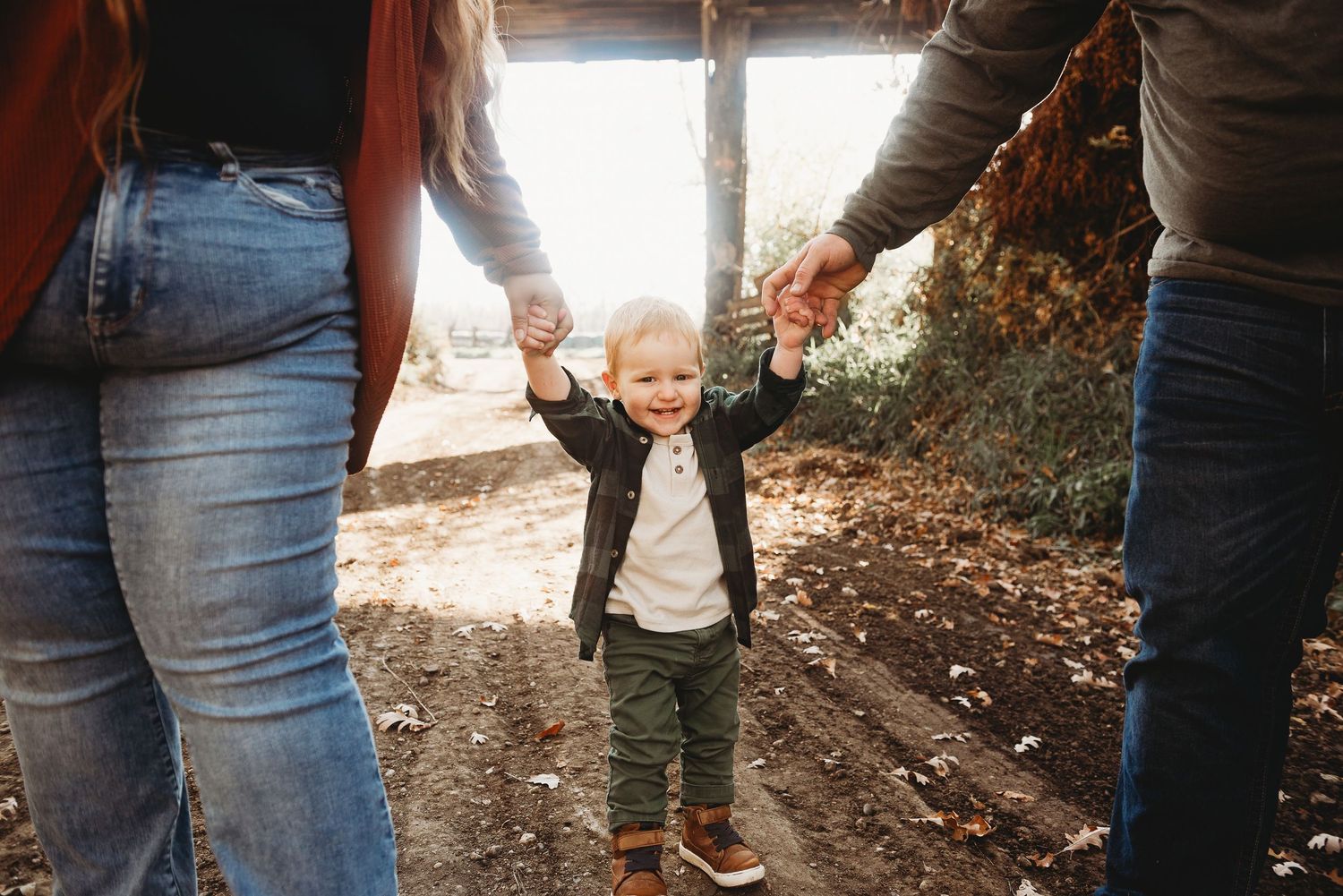 Jumping and skipping with mom and dad, a little one smiles big during an outdoor family session at sunrise along the north side of mandan