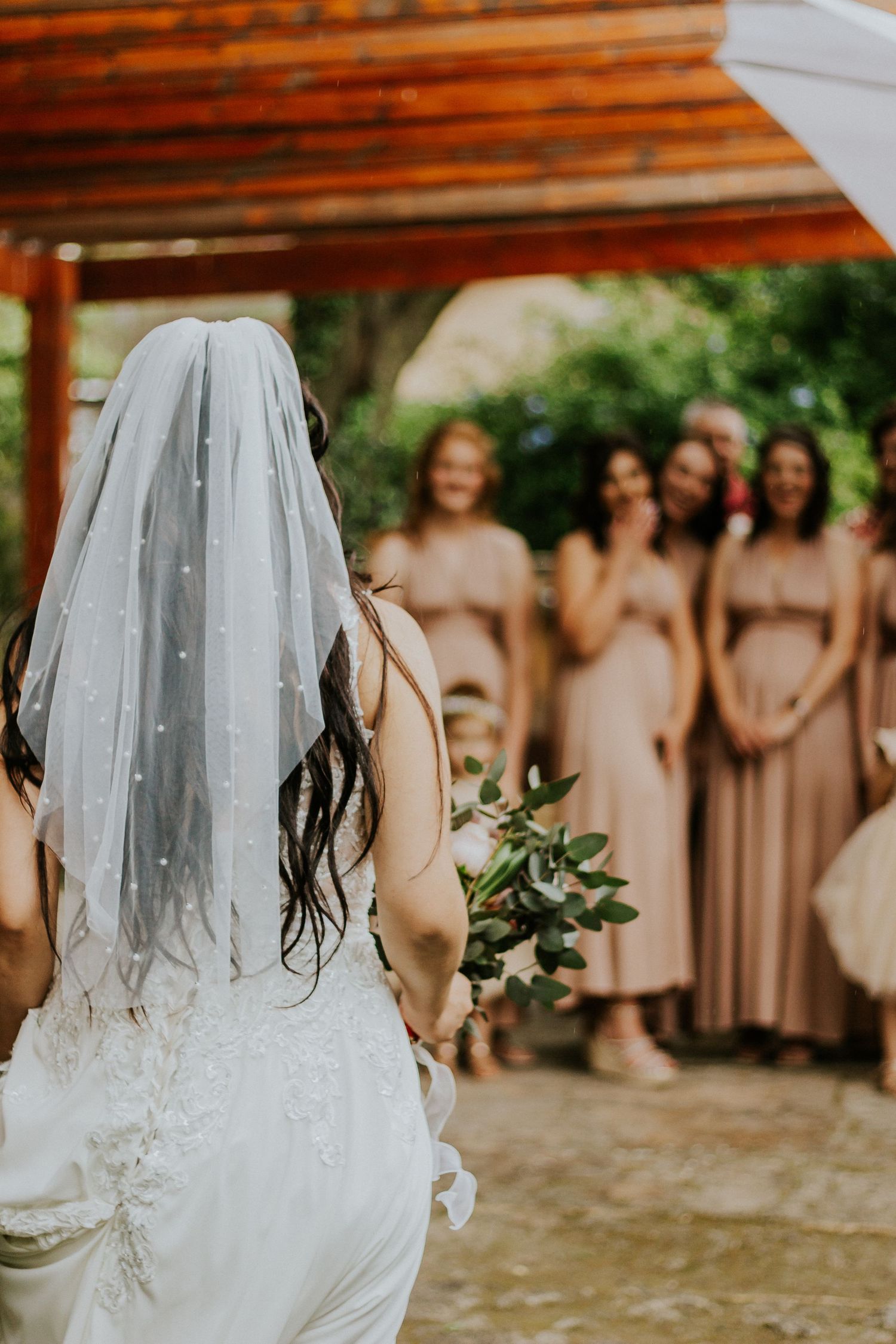 Candid wedding photography of a bride walking toward her bridesmaids holding bouquets.