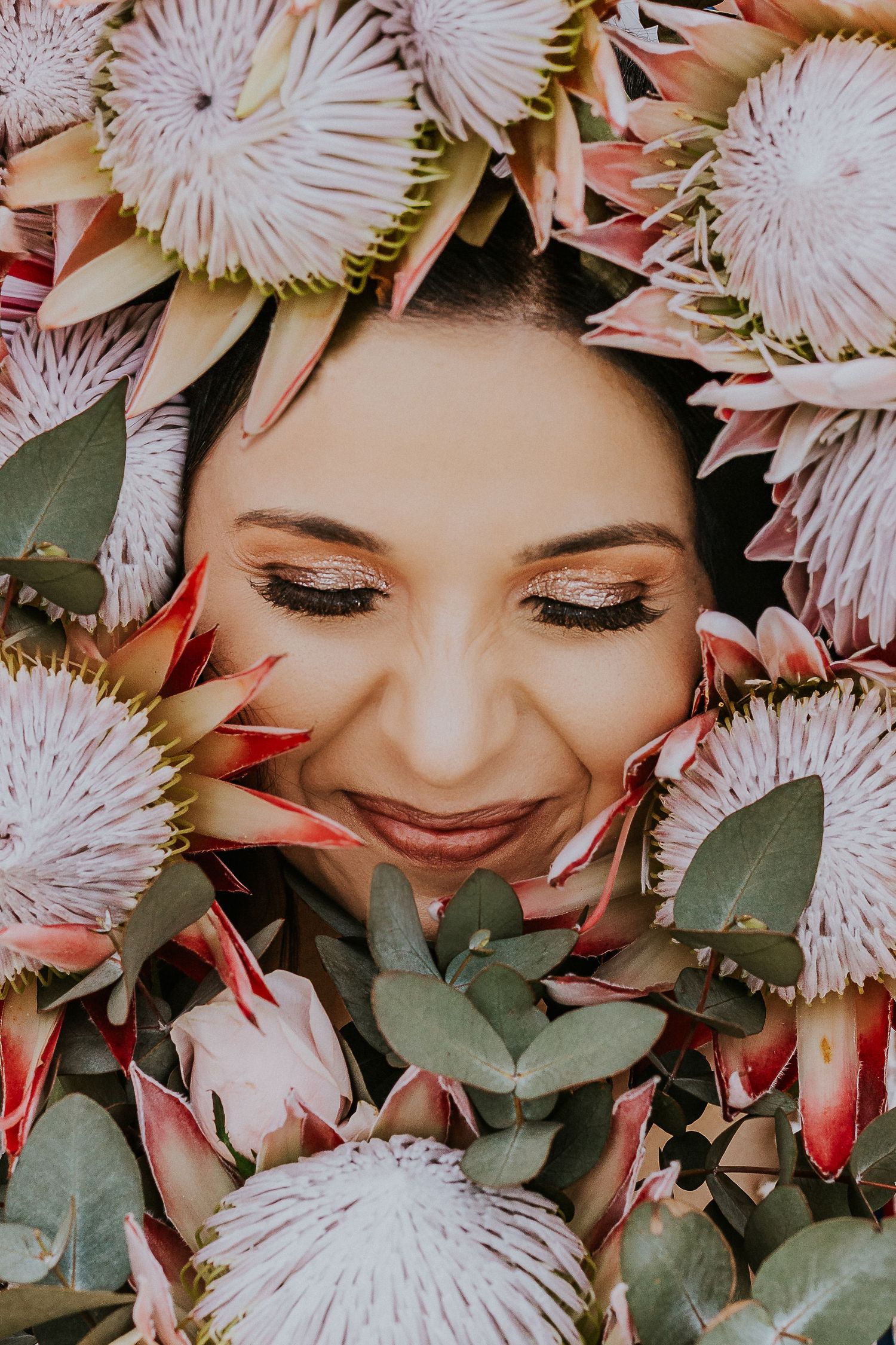 Artistic bridal portrait of a bride looking down, framed by beautiful King Proteas.