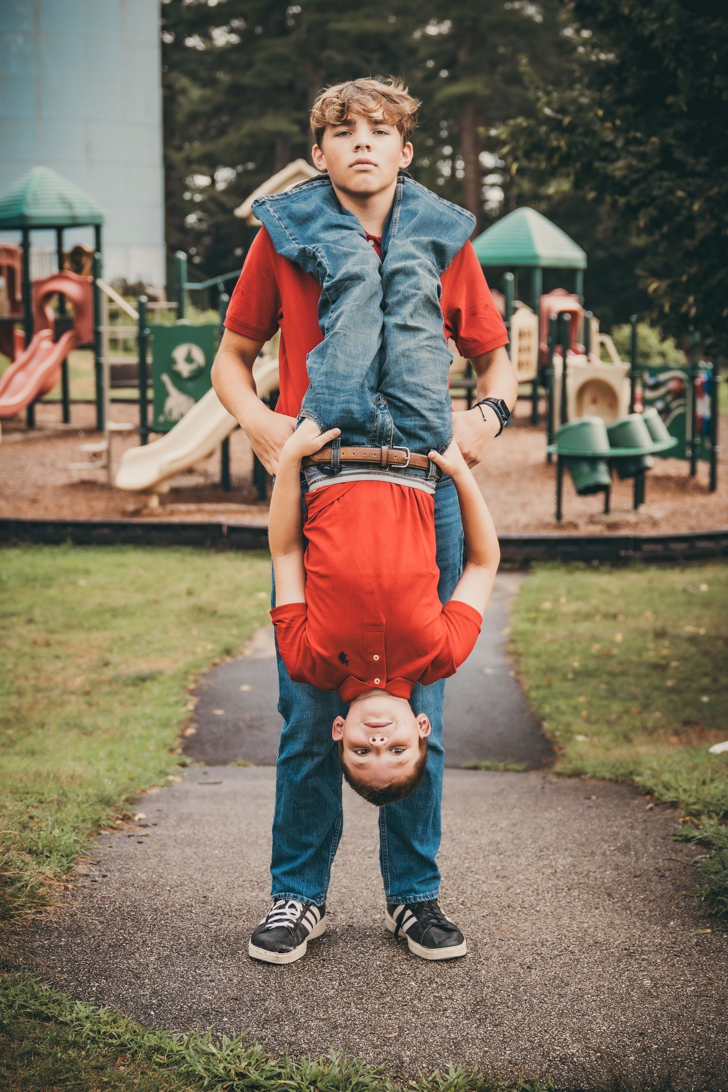 Children playing and doing handstands on a paved pathway at a playground.