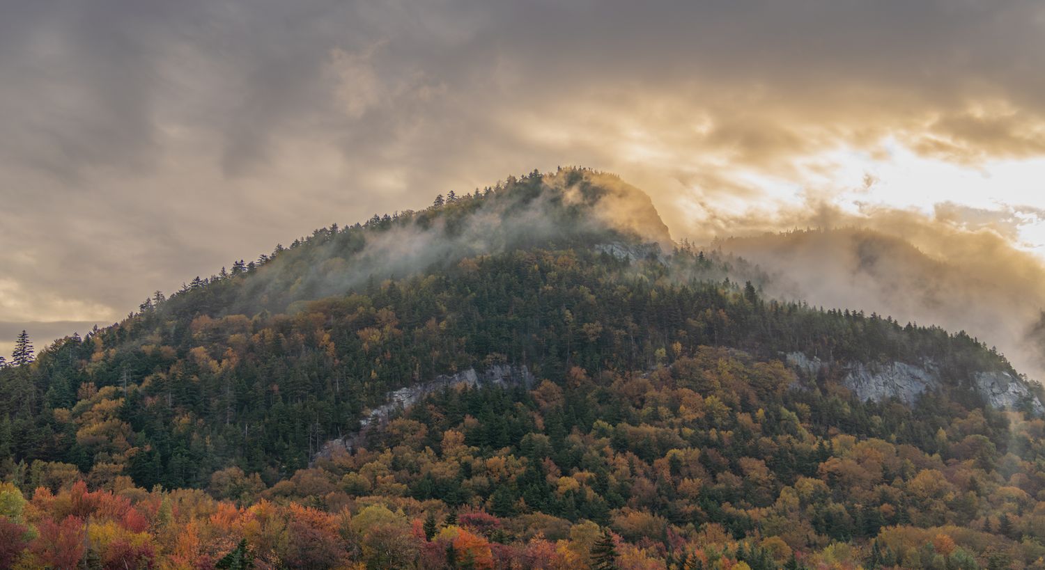Mountain landscape with misty peaks and autumn colors during golden hour.