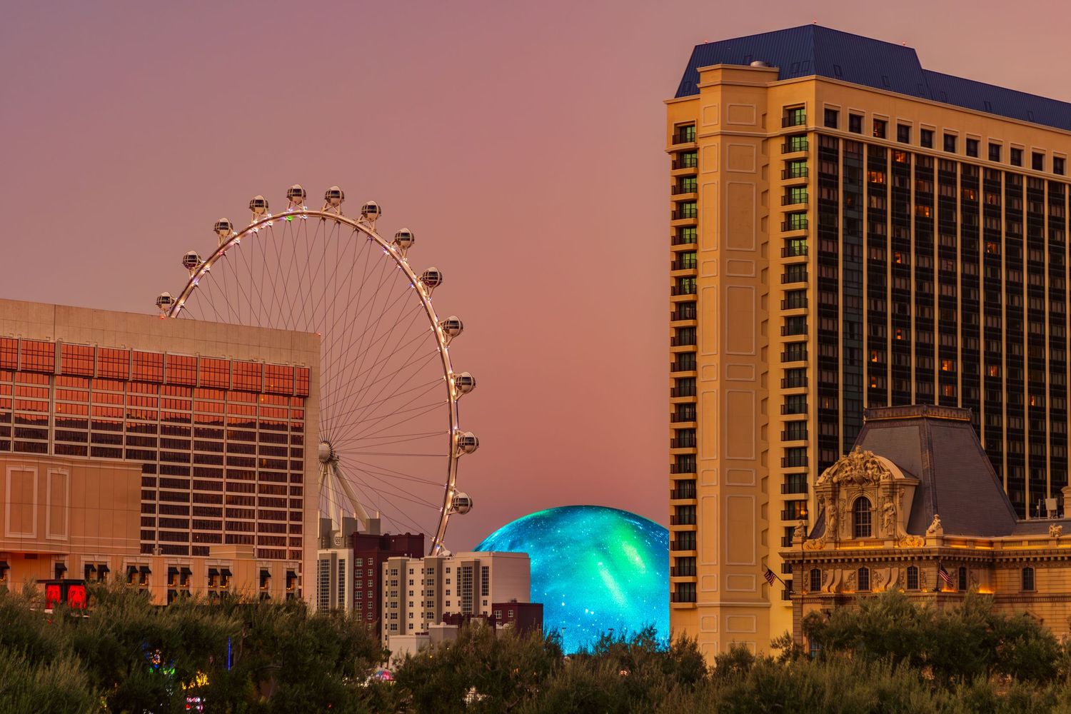 Las Vegas Strip skyline at dusk with illuminated hotels and Ferris wheel against pink sky.