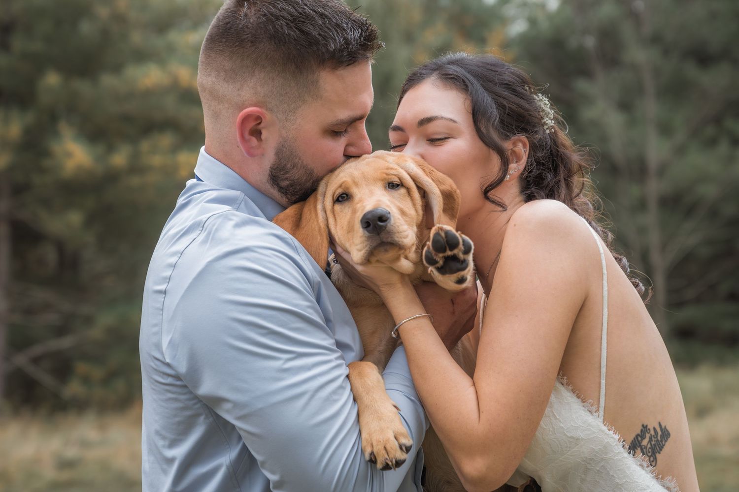 A couple shares an intimate moment outdoors with their golden retriever.