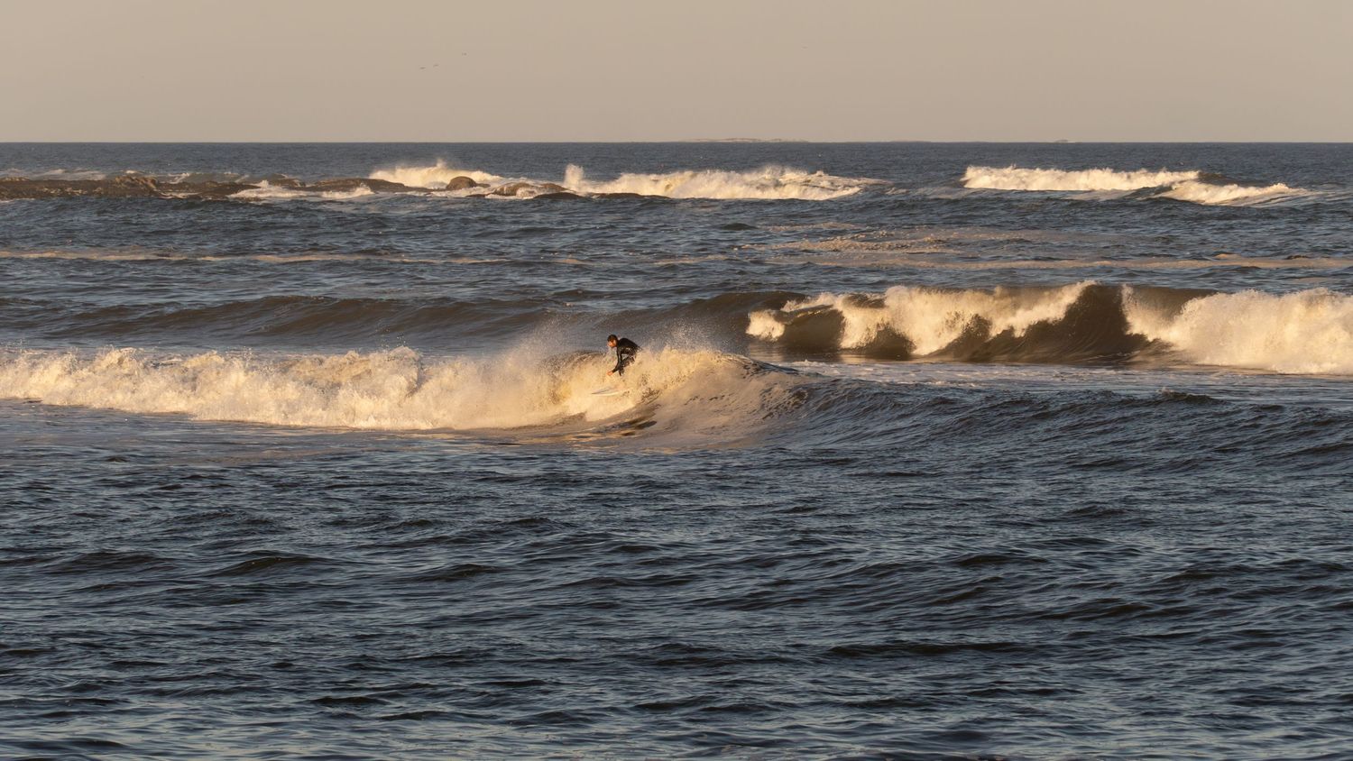 Surfer rides a wave during golden hour on a choppy ocean with dramatic white surf.