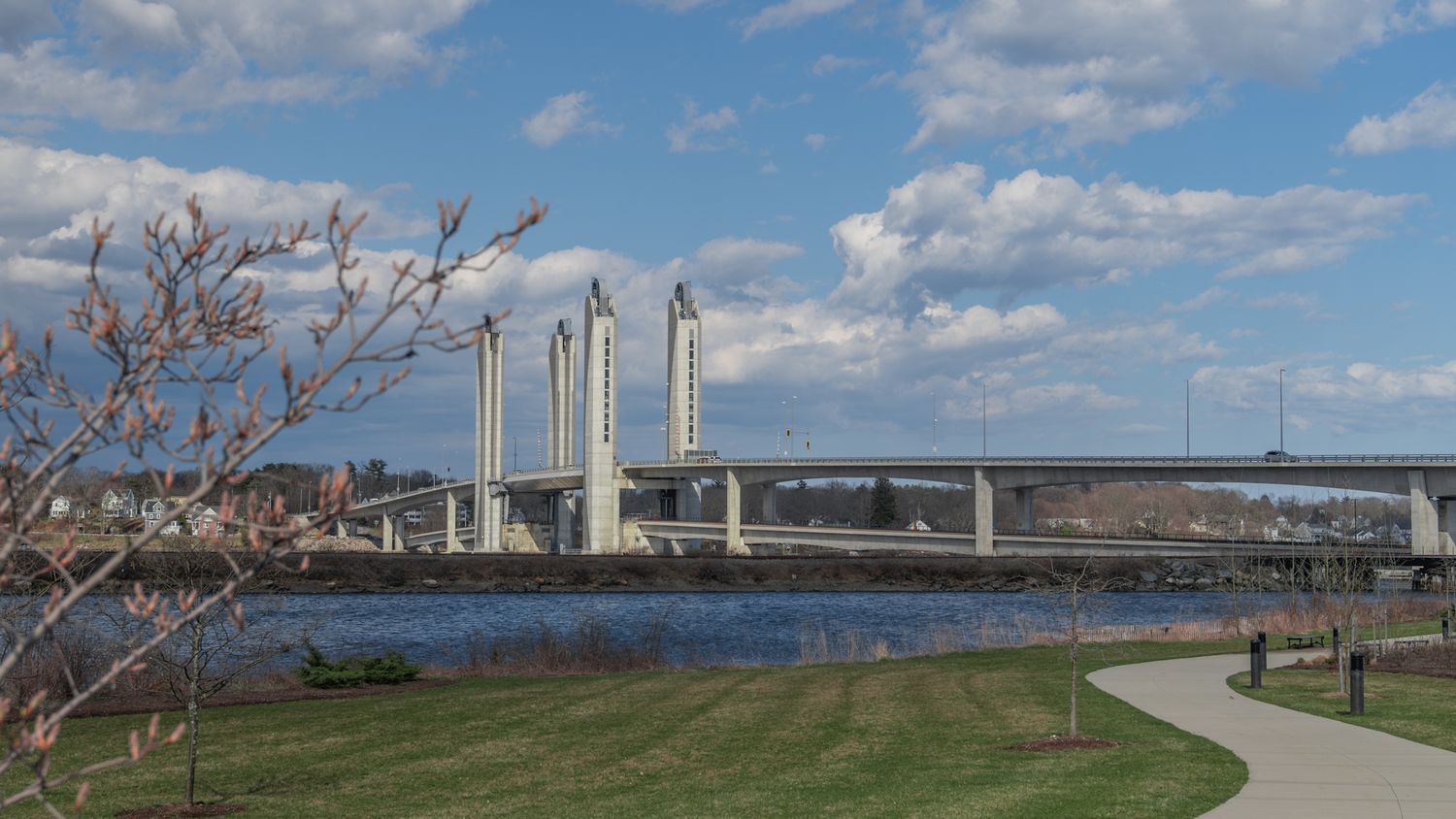 Coastal walkway with wind turbines and bridge spanning across blue water on sunny day.