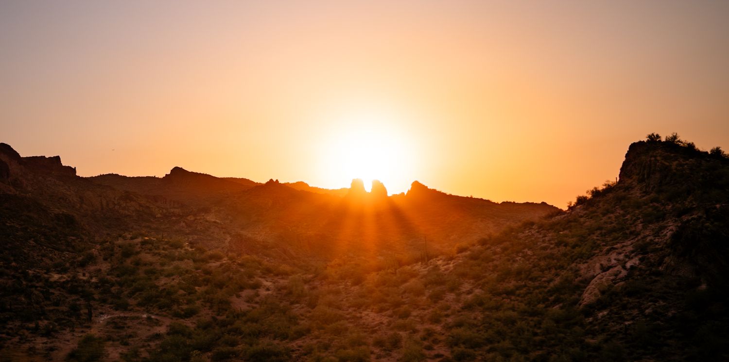 Golden sunset silhouetting a rocky coastline with lighthouse in warm orange hues.