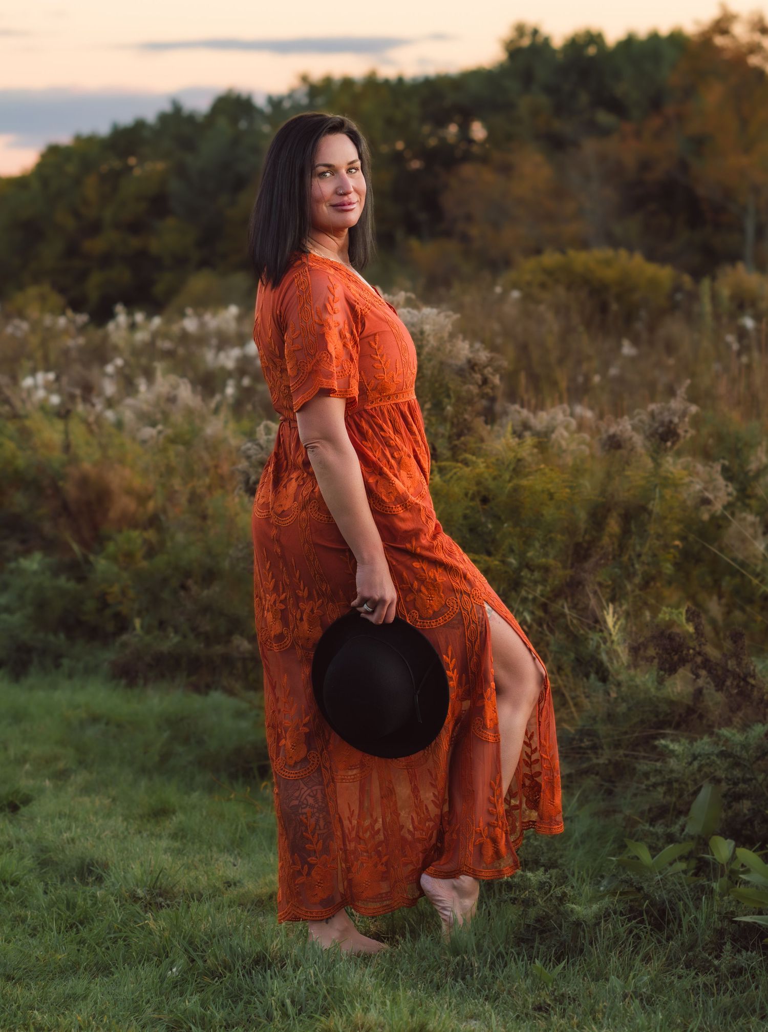 Woman in orange lace dress posing in a natural outdoor setting at sunset.