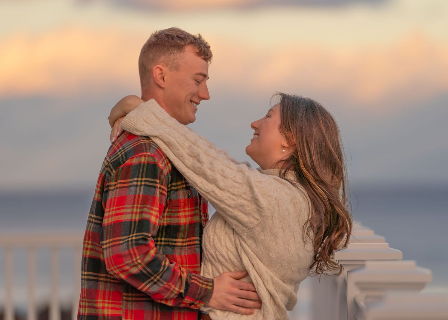 A romantic couple embraces during golden hour with warm sunset lighting.