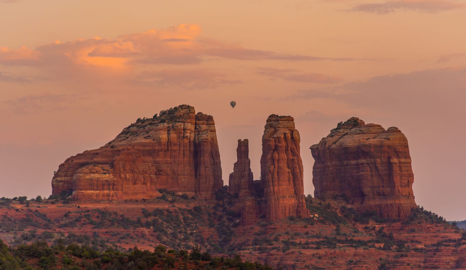 Red rock formations of Sedona illuminated by warm sunset light against a pink sky.
