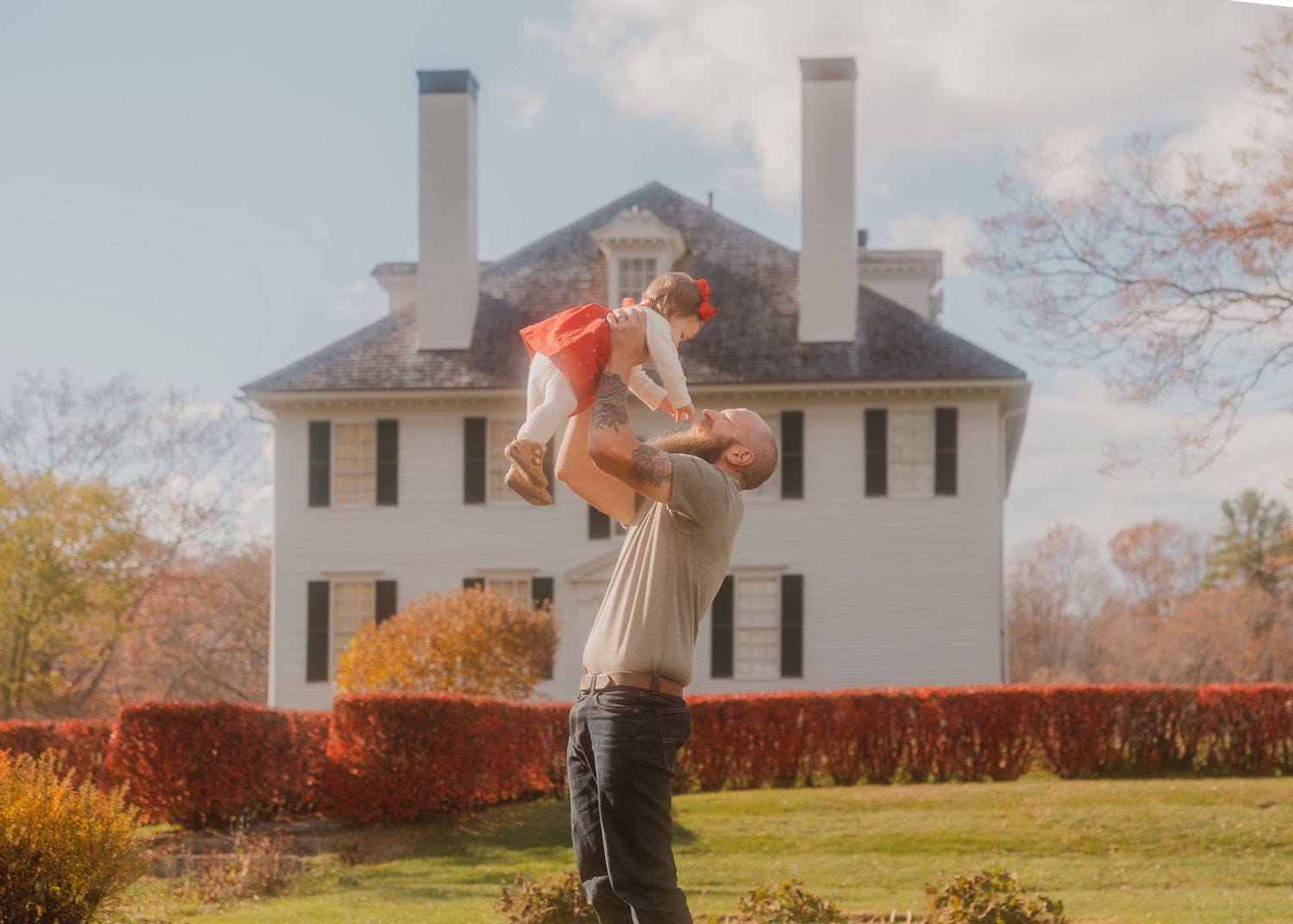 A joyful moment of play in front of a white colonial house with chimneys.