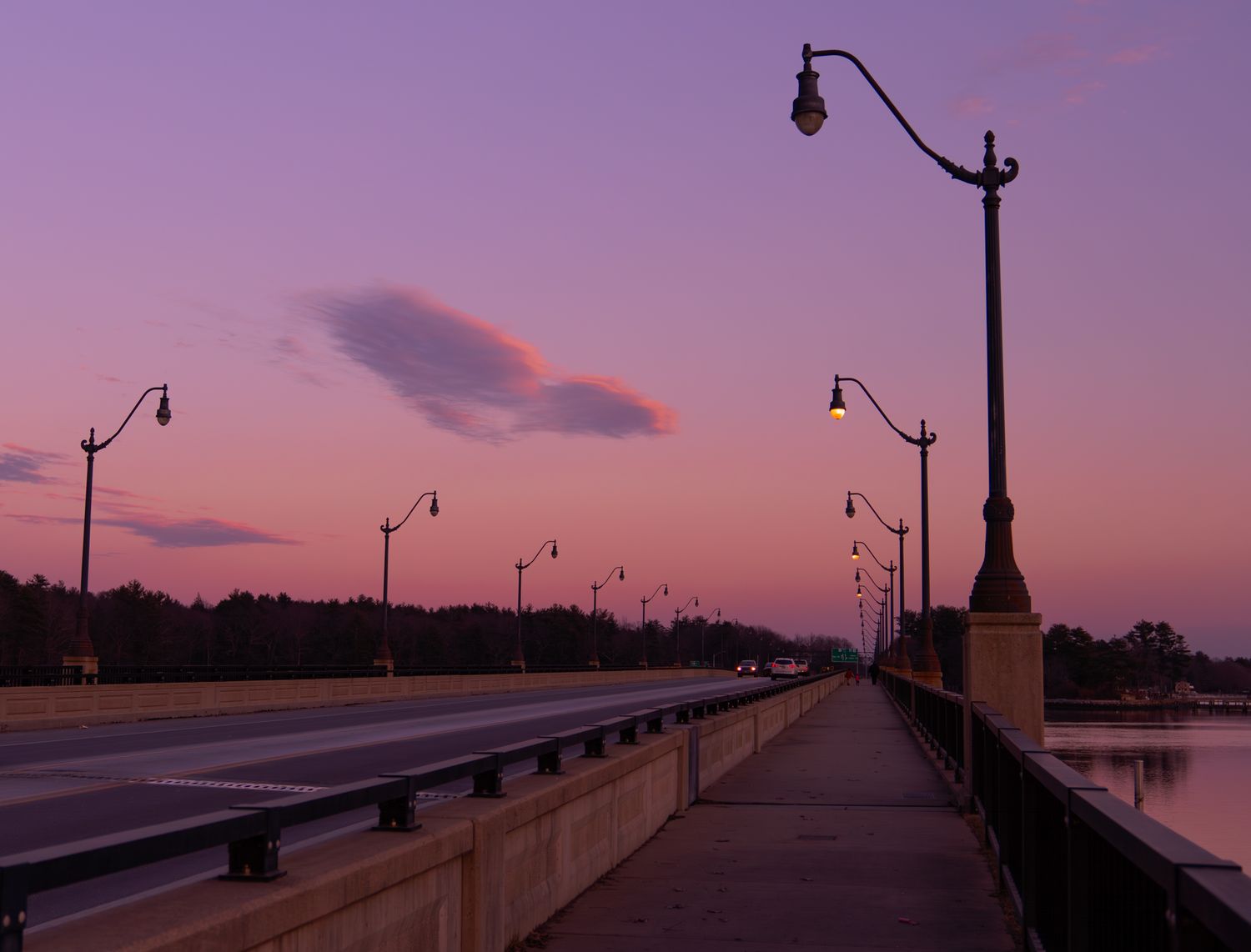 Scenic boardwalk with lamp posts along a waterfront during a vibrant purple sunset.