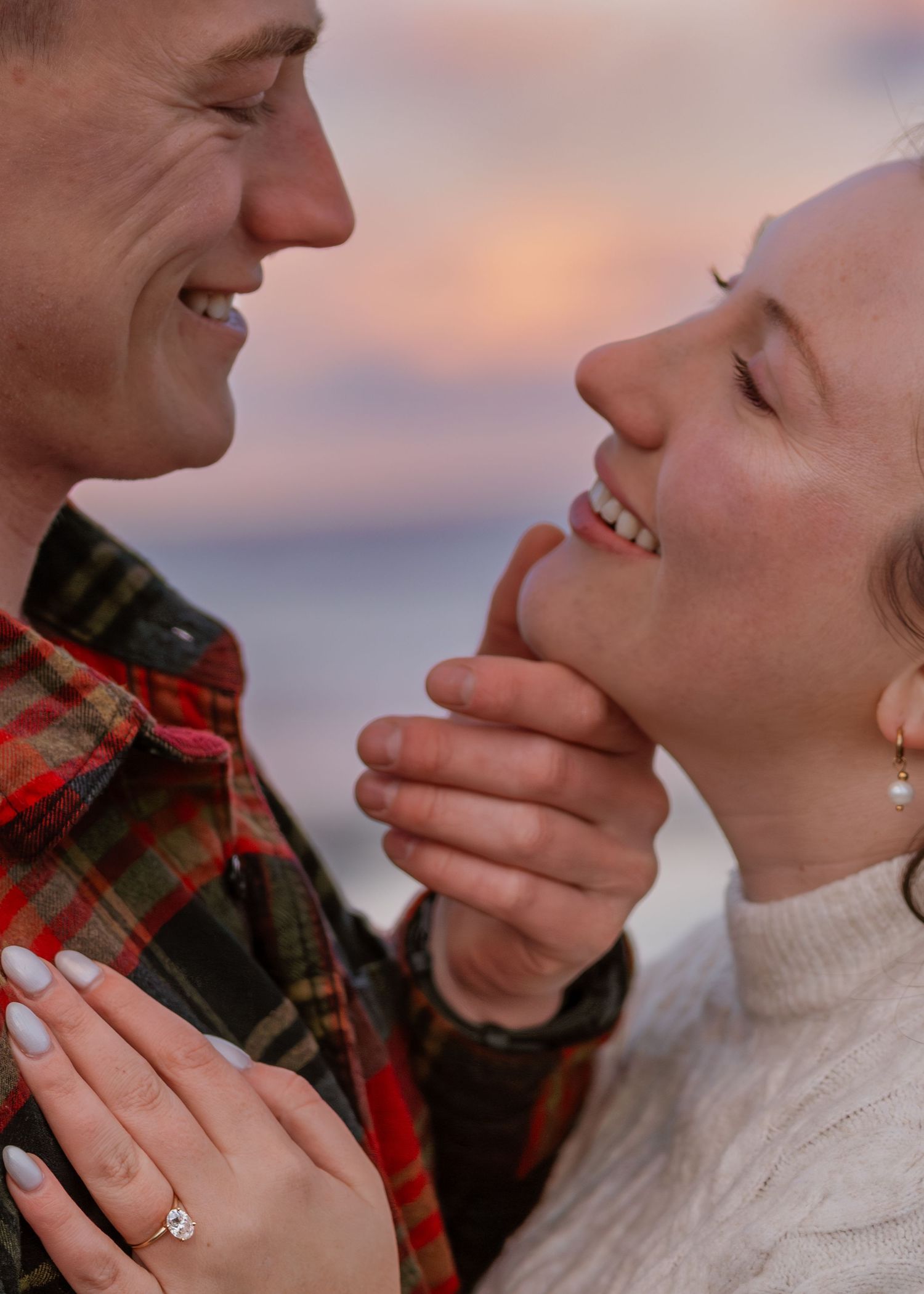 Intimate engagement moment captured during sunset with hands tenderly touching face.